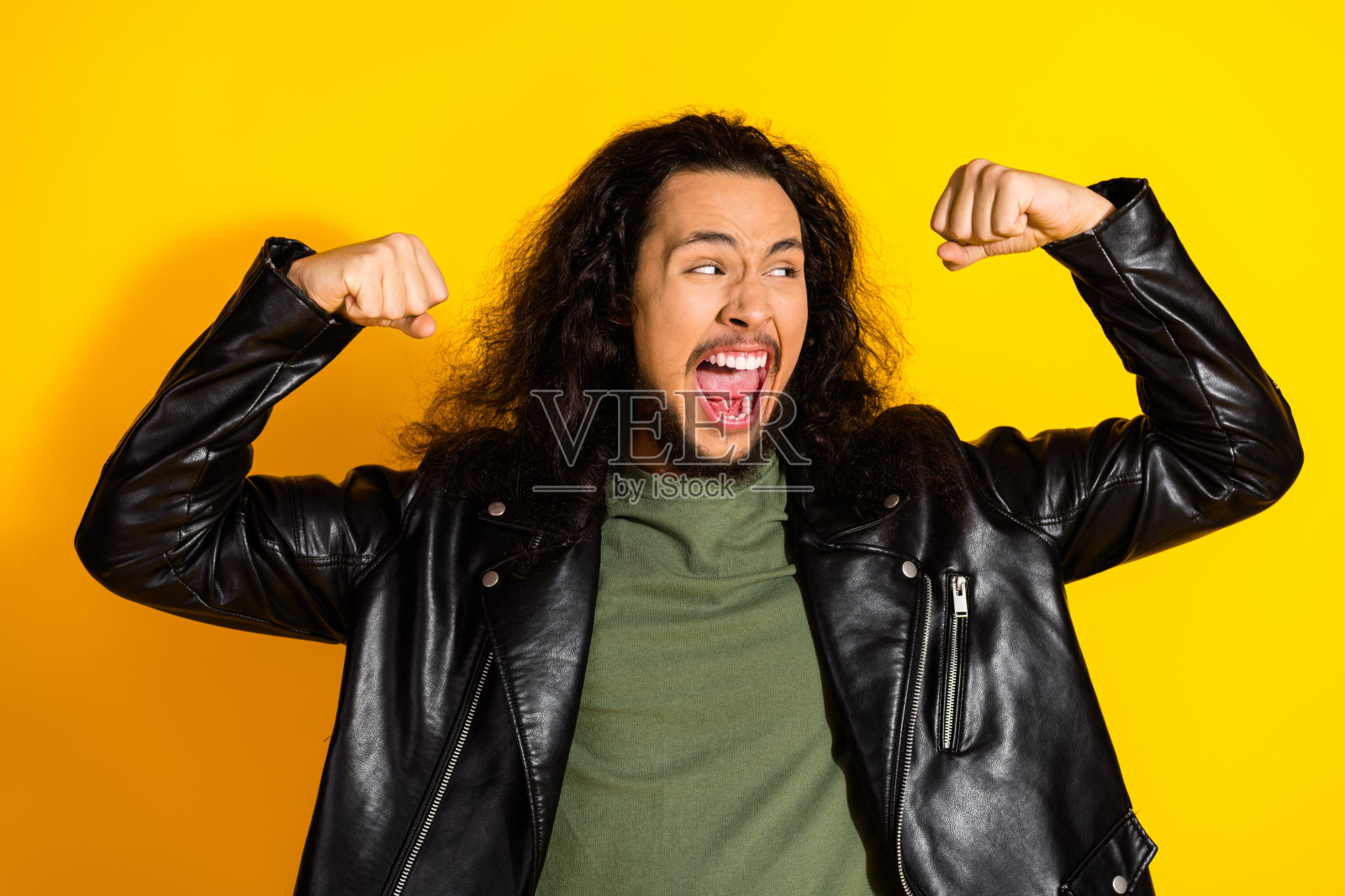 年轻男子穿着皮夹克，在明亮的黄色背景下兴奋地展示手臂，散发出风格、自信和活力。照片摄影图片
