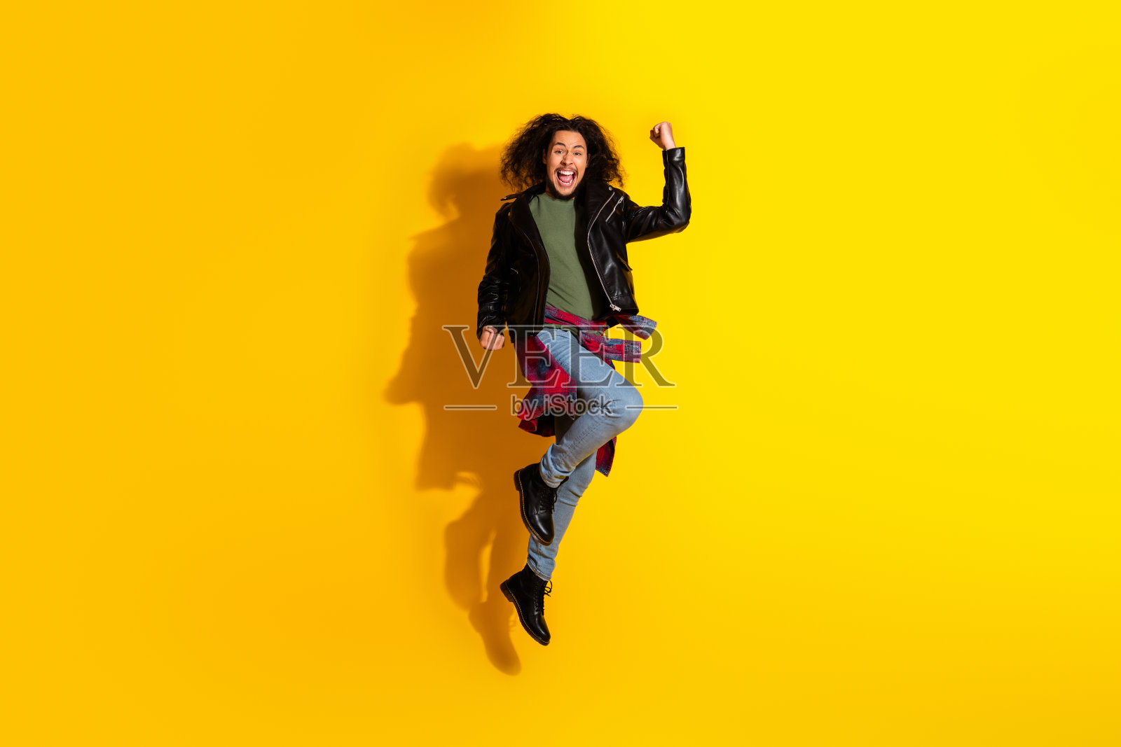 充满活力的年轻男子在鲜艳的黄色背景上跳跃，面带快乐的表情，展示时尚与风格照片摄影图片