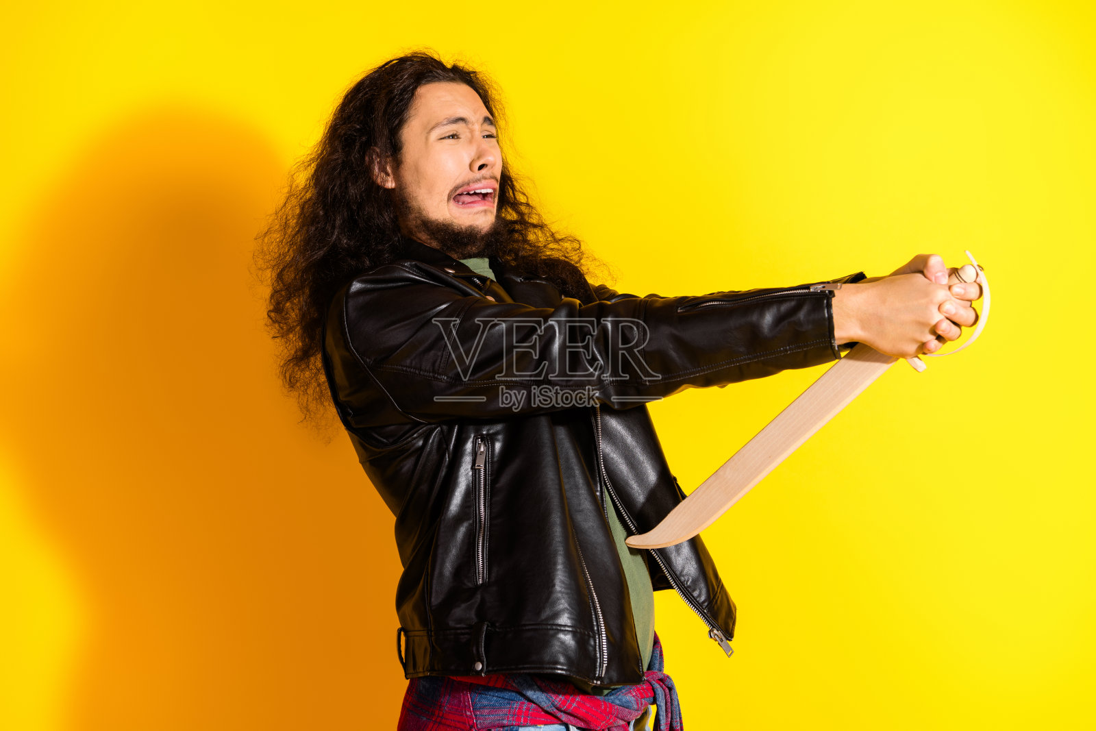 身穿黑色皮夹克的年轻男子在鲜艳的黄色背景前摆出富有表现力的姿势，强调个性。照片摄影图片