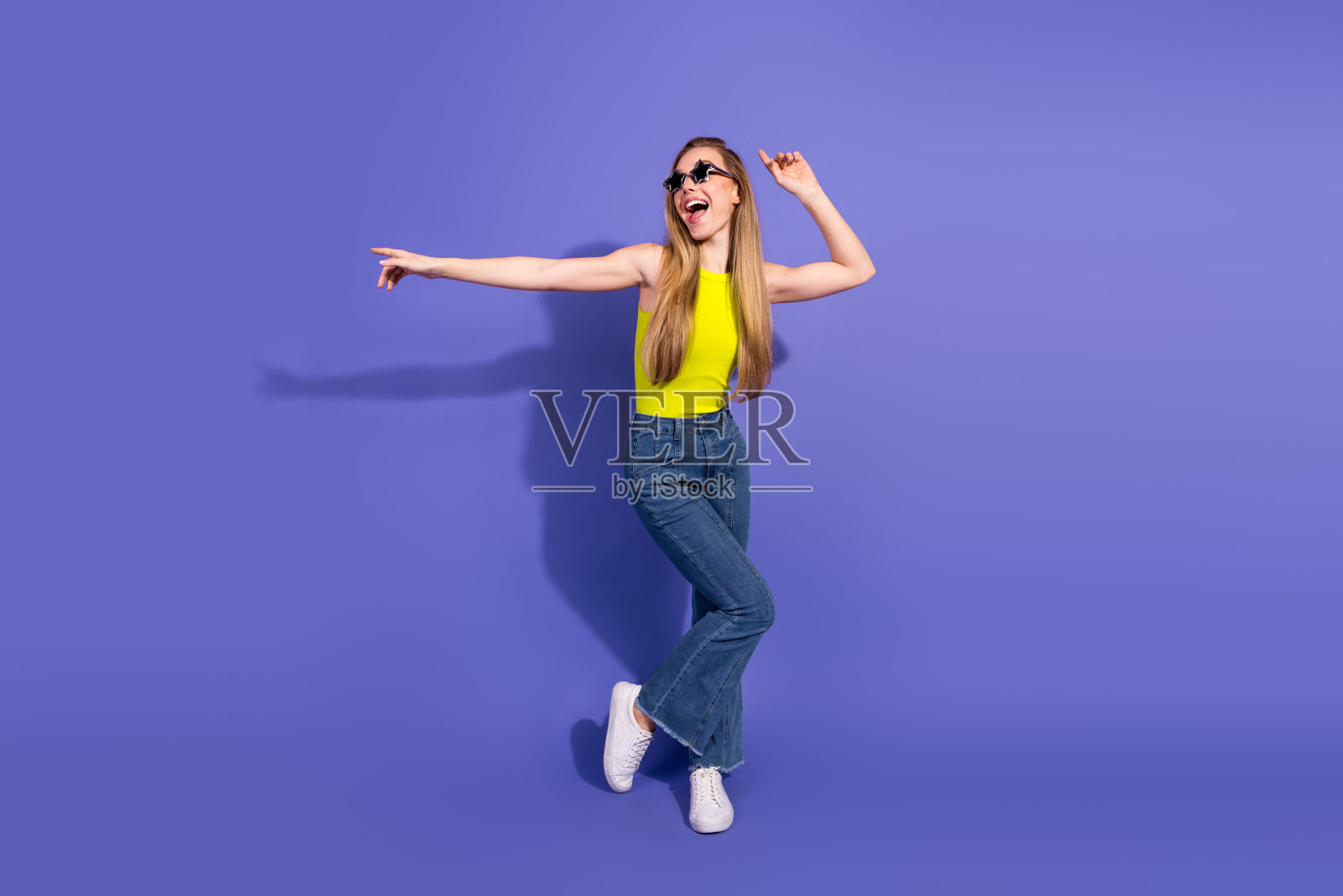 穿着活力黄色上衣的年轻女性在紫色背景下快乐地跳舞，享受乐趣并表达幸福。照片摄影图片