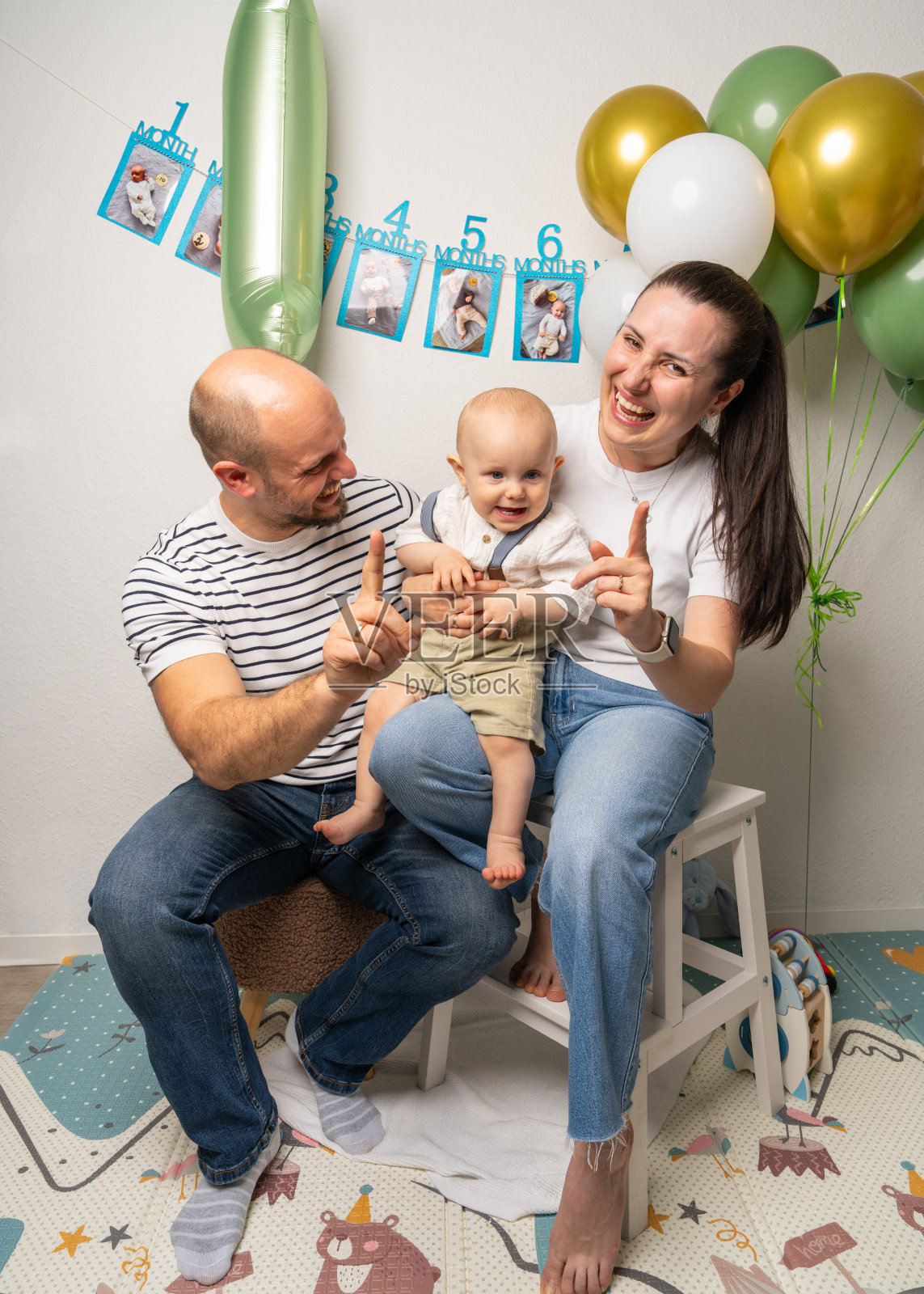 快乐的家庭抱着他们微笑的一岁男孩，调皮地用手指展示数字一。欢快的时刻庆祝宝宝的第一次生日和家庭的爱。照片摄影图片