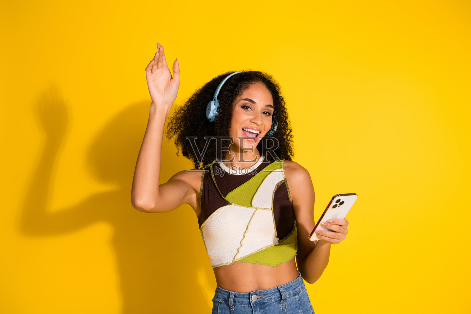 时尚年轻女性在充满活力的黄色背景下，戴着耳机享受音乐，同时手持手机。照片摄影图片