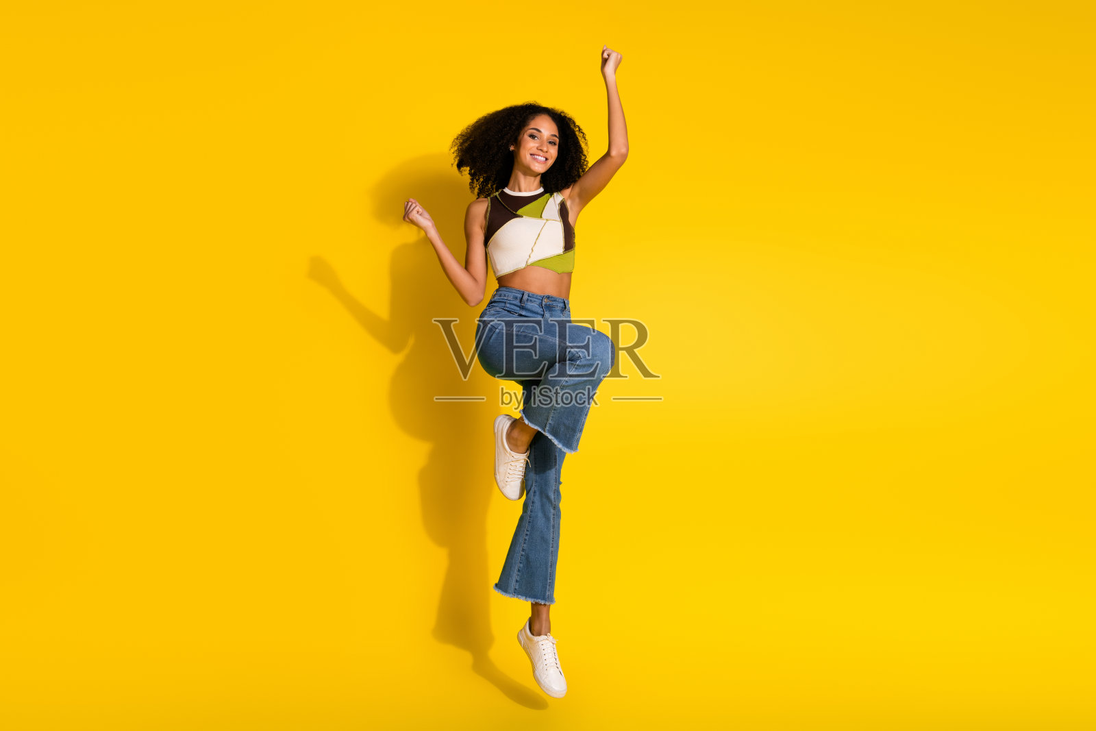 快乐的女性在充满活力的黄色背景下跳跃，表达着幸福和乐趣照片摄影图片
