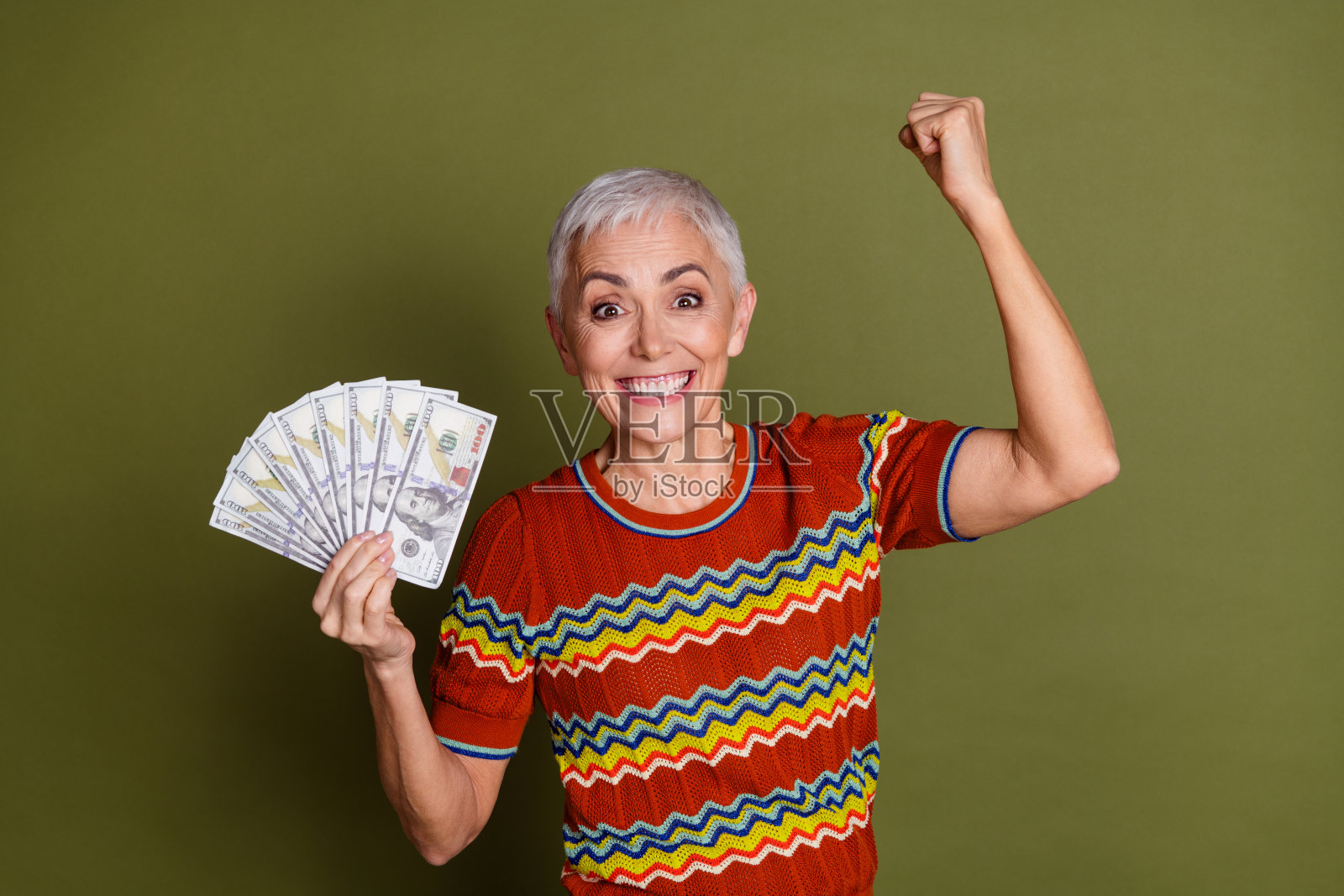 微笑并庆祝成功的老年女性，手持现金，背景为绿色照片摄影图片