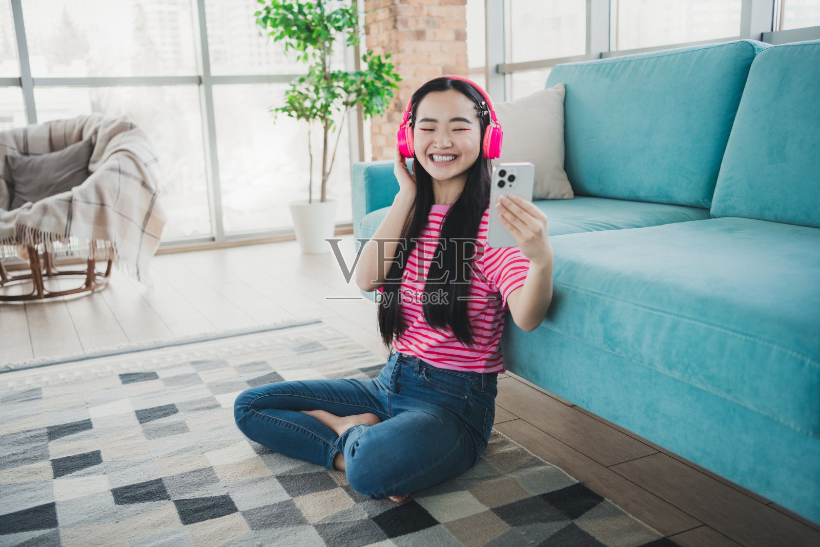 年轻女性在阳光明媚的日子里，戴着耳机在舒适的客厅里享受音乐，同时自拍。照片摄影图片