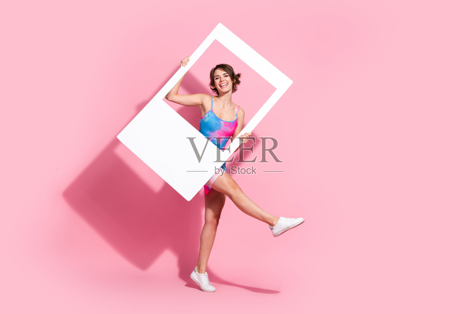 迷人的年轻女性穿着鲜艳的夏季服装，手持一个框架，背景为粉色。照片摄影图片