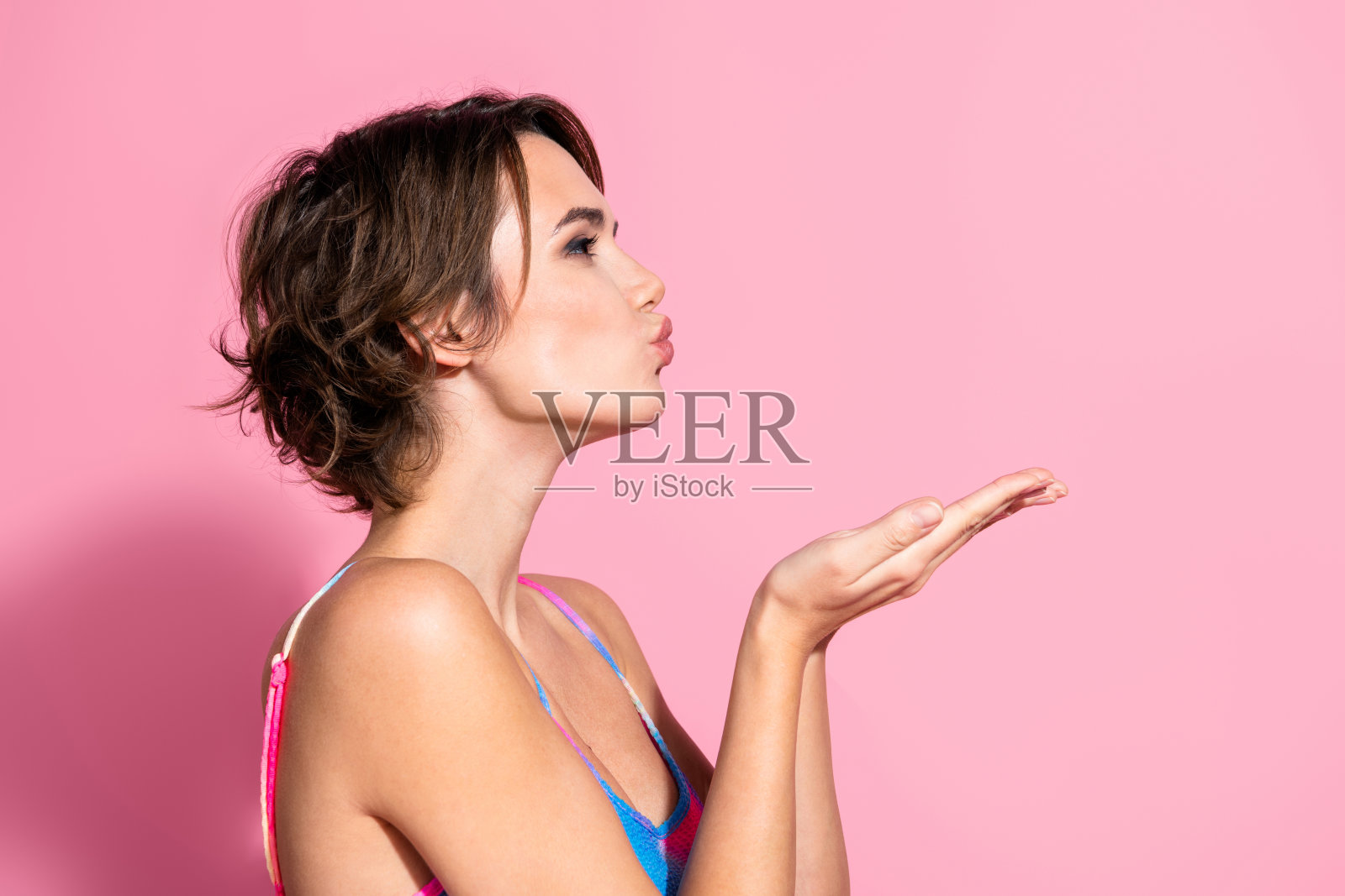 年轻女性穿着夏季连衣裙在粉色背景前送吻照片摄影图片