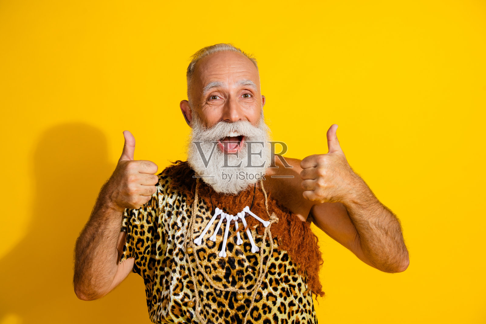 古老的穴居人穿着豹纹衣服，竖起大拇指，背景为黄色。照片摄影图片