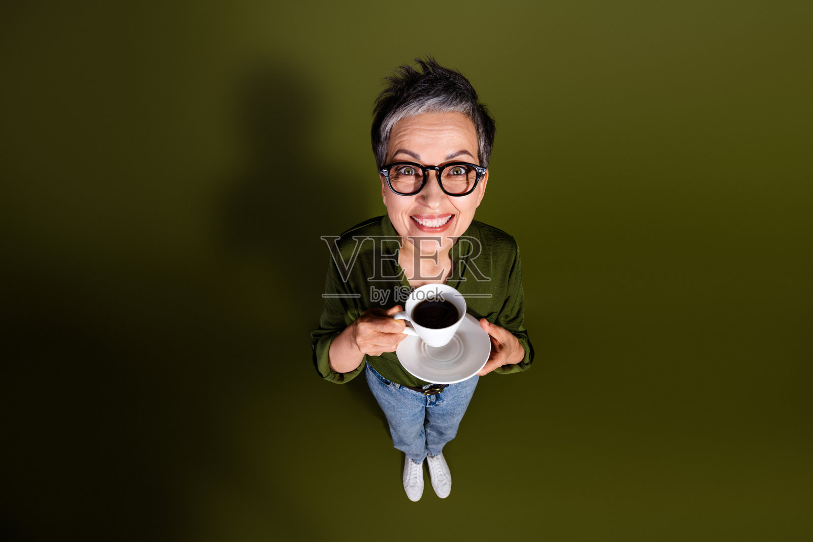 微笑的成熟的女性戴着眼镜，手握咖啡杯，穿着休闲，短发灰色，从上方俯视，享受愉快的时刻。照片摄影图片