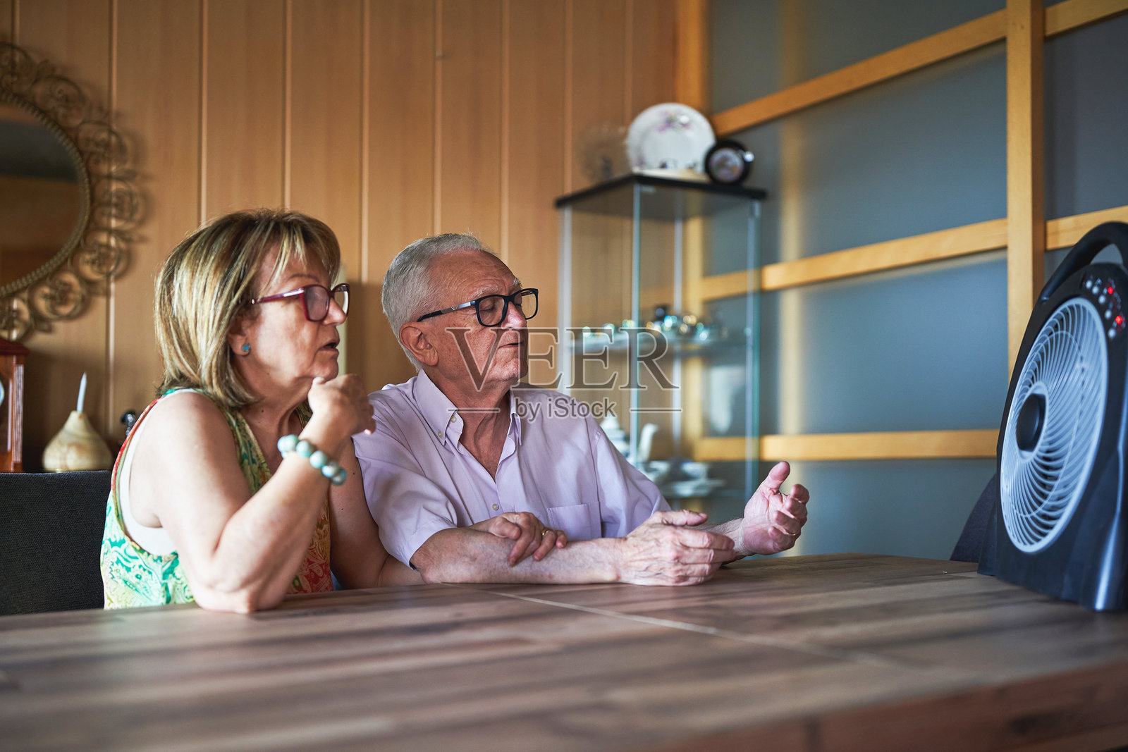 一对老年夫妇在家中用风扇降温，度过热浪。照片摄影图片