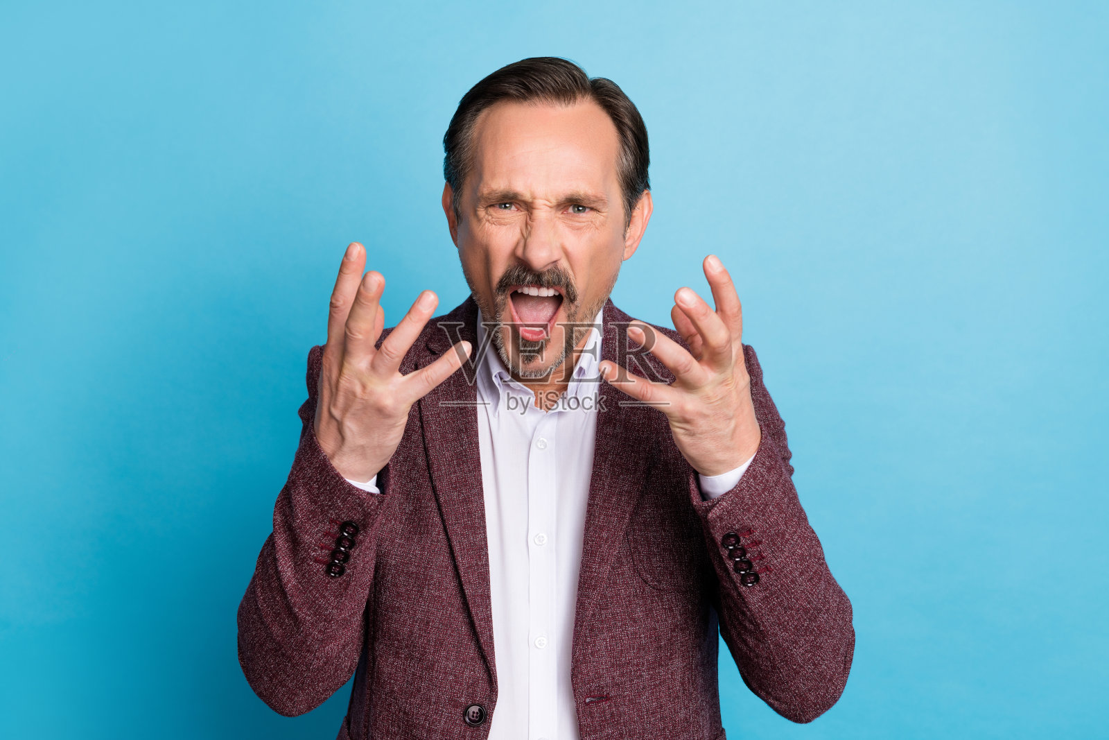 愤怒的老板不满的面孔，尖叫着“你被解雇了”，穿着红色西装外套，背景为蓝色。照片摄影图片