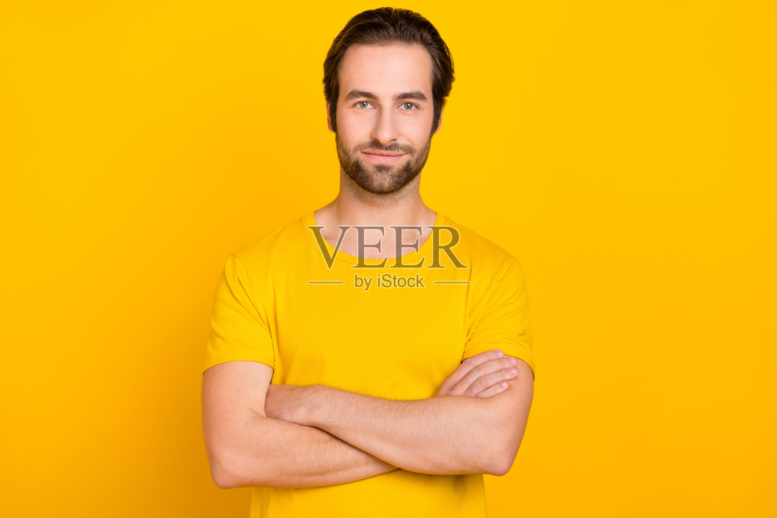 年轻男士穿着休闲服，双手交叉，像个聪明的代理人，背景为黄色。照片摄影图片