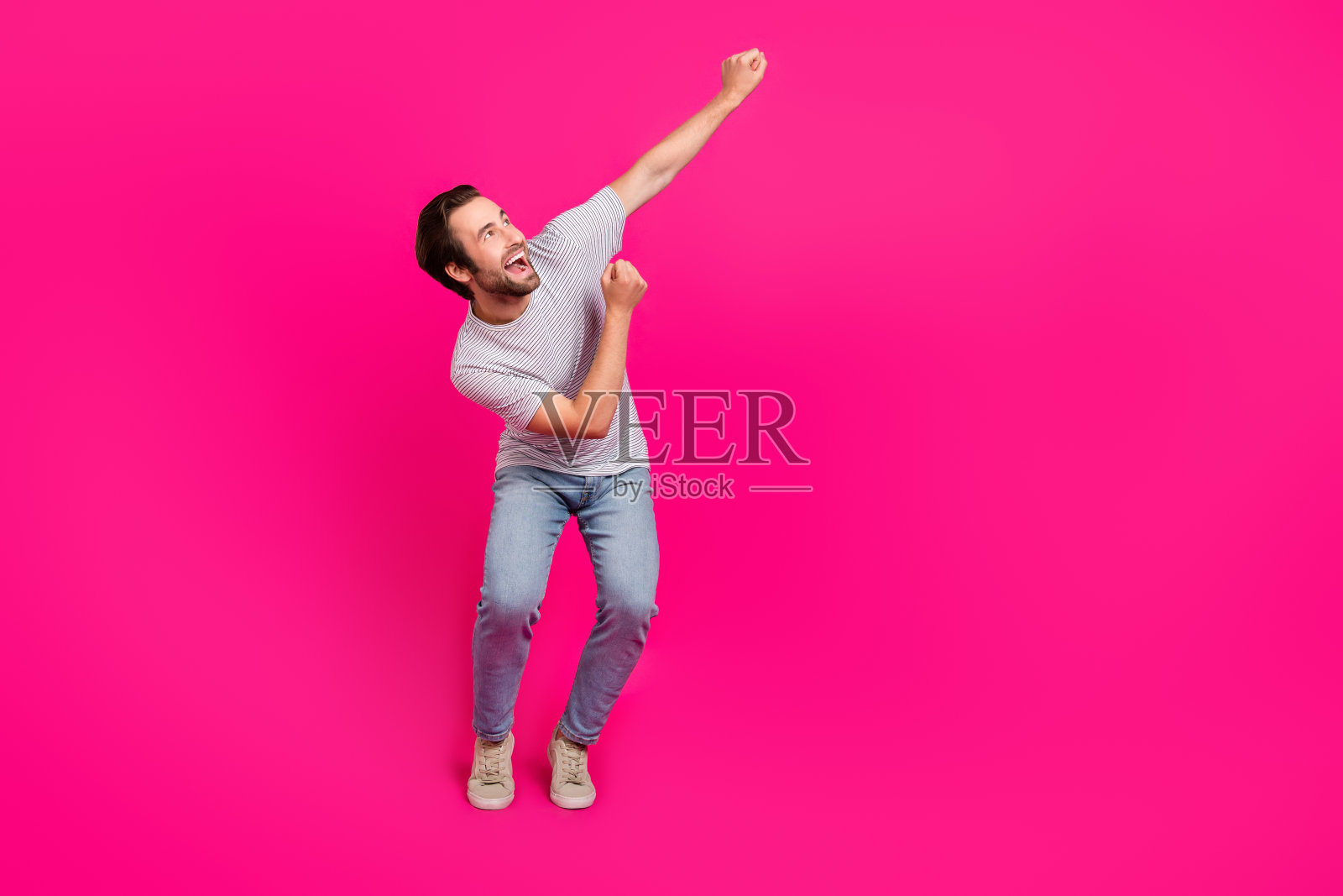 年轻快乐的男孩在品红色背景下庆祝胜利，目光投向空旷的空间。照片摄影图片