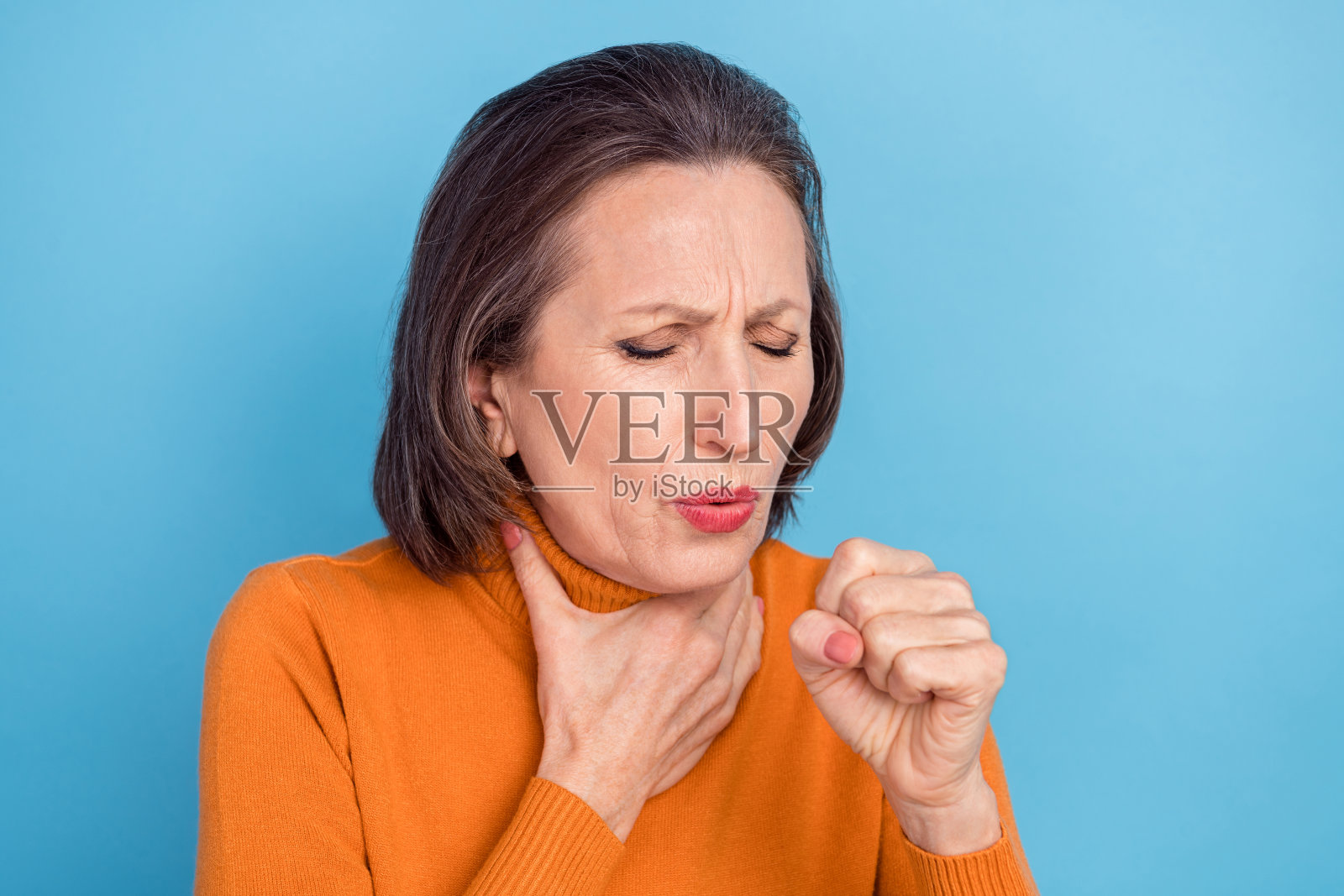 不满的老年女性肖像，手臂触碰脖子，握拳咳嗽，感觉不适，背景为蓝色。照片摄影图片