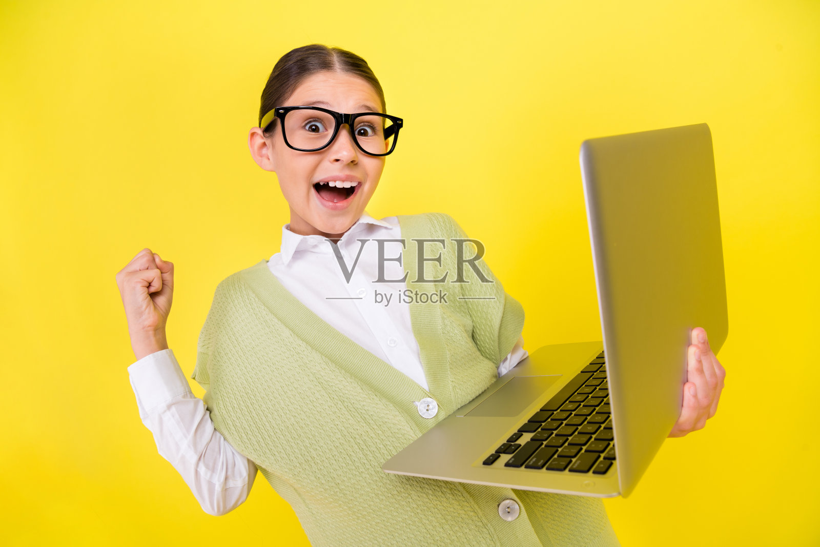 迷人的时尚女孩在明亮的黄色背景下，惊喜地使用笔记本电脑，庆祝她的网络项目。照片摄影图片