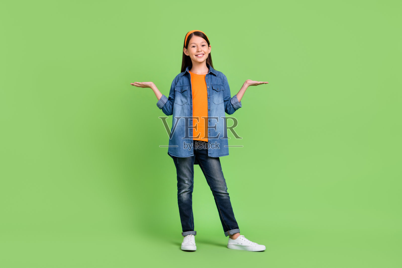 全身照，搞笑的青春期女孩手牵手，穿着衬衫、牛仔裤、发带和鞋子，背景为绿色。照片摄影图片