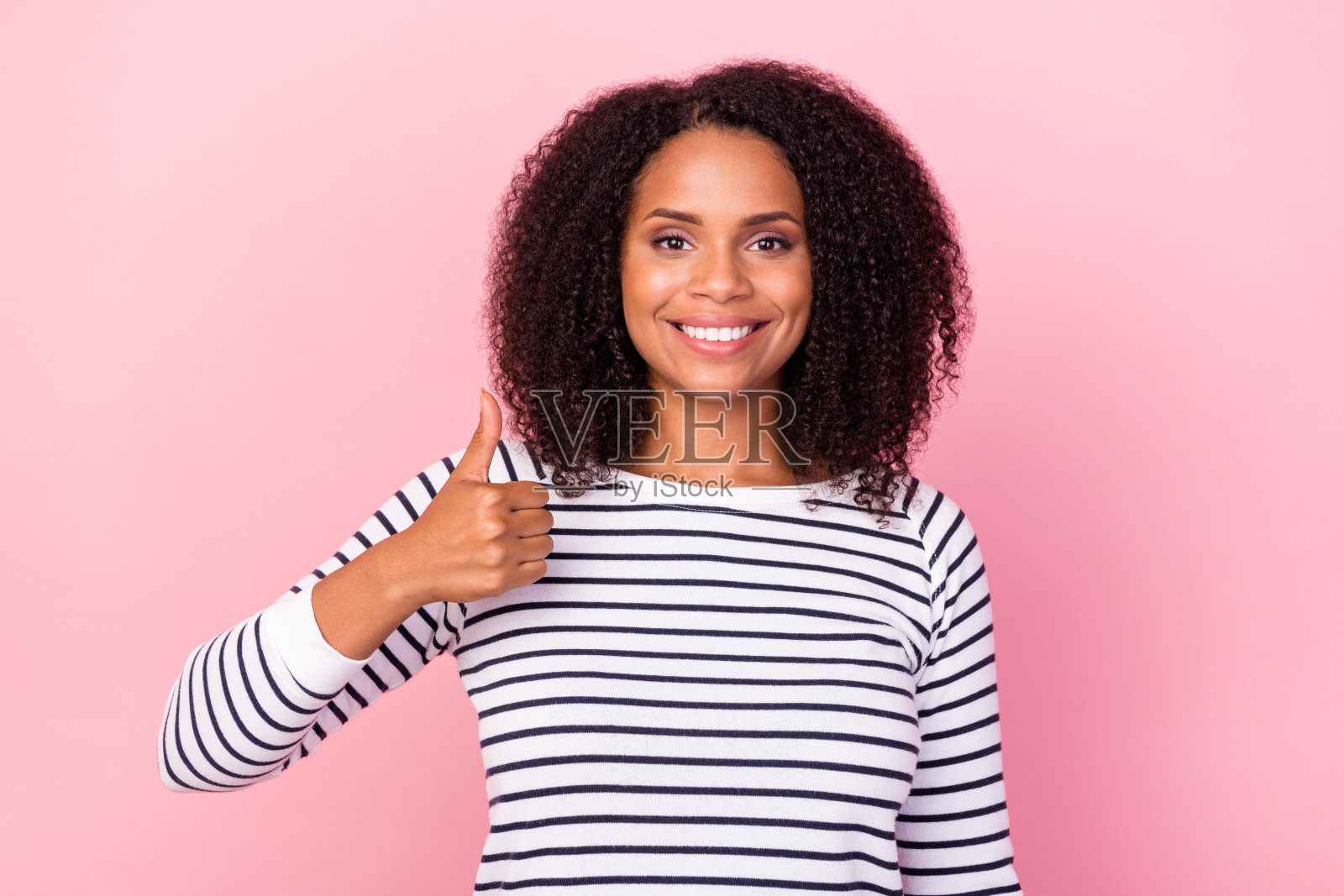 一位开心的女士在粉色背景下露出灿烂的笑容并竖起大拇指。照片摄影图片