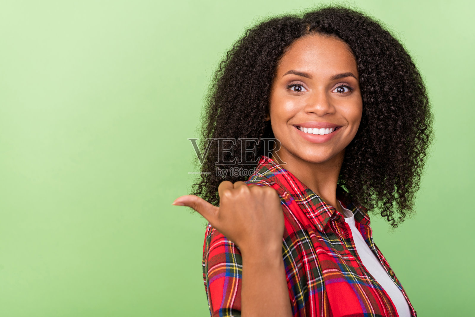 年轻非洲女孩侧面肖像，手指指向空白区域，适合选择促销广告，背景为绿色。照片摄影图片