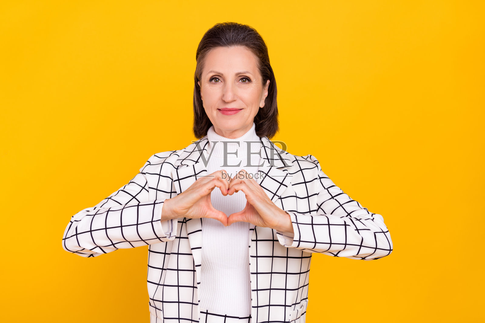 一位满意的女士在黄色背景下用手指做出心形符号的肖像。照片摄影图片