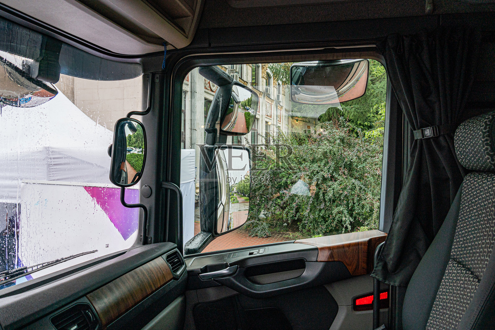 昏暗的卡车驾驶室内部透过窗户可以看到热闹的街景。图像中有黑色座椅、方向盘、人群、建筑物和城市中的一棵树。颜色是照片摄影图片