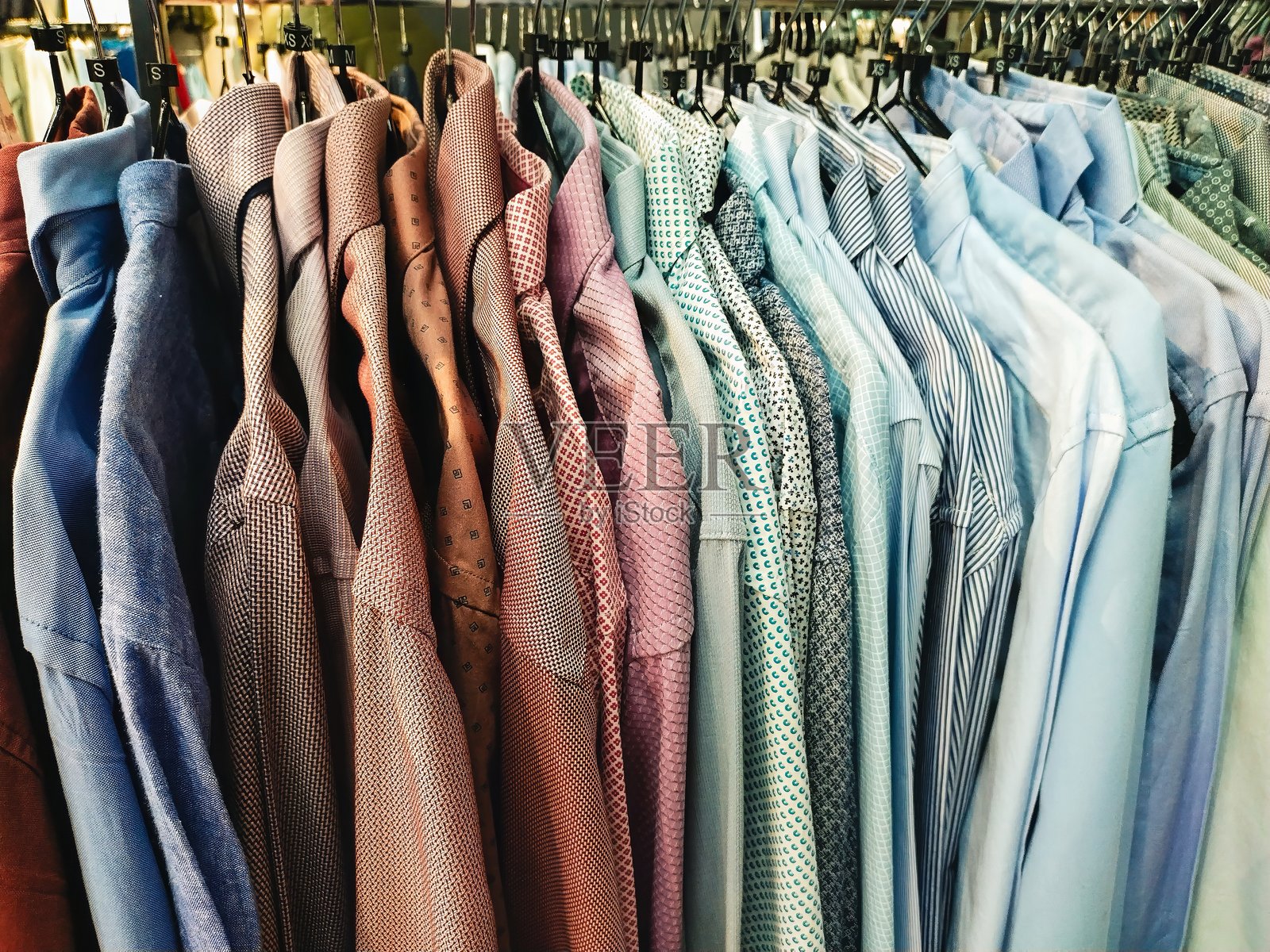 不同颜色和图案的衬衫挂在架子上，准备在服装店出售。照片摄影图片