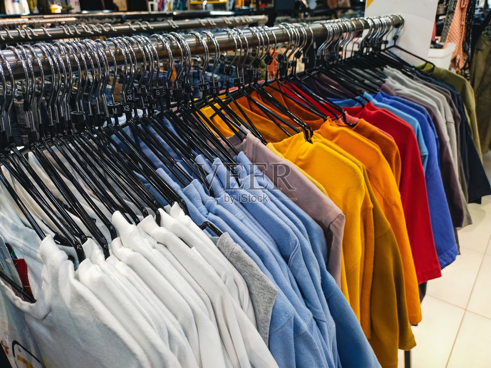 五颜六色的T恤在服装店的货架上展示，准备供顾客浏览和购买。照片摄影图片