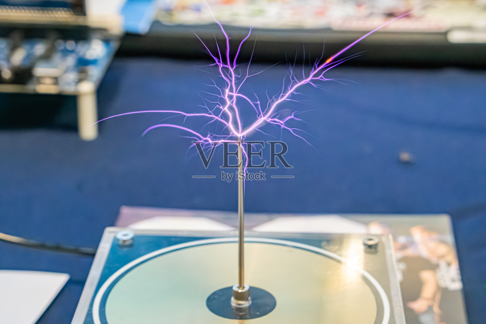 室内环境中，电器设备在蓝色表面上发出紫色和白色火花，可能是工作台。背景中有电子元件或电路的绿色电路板，旁边是一个唱盘。照片摄影图片