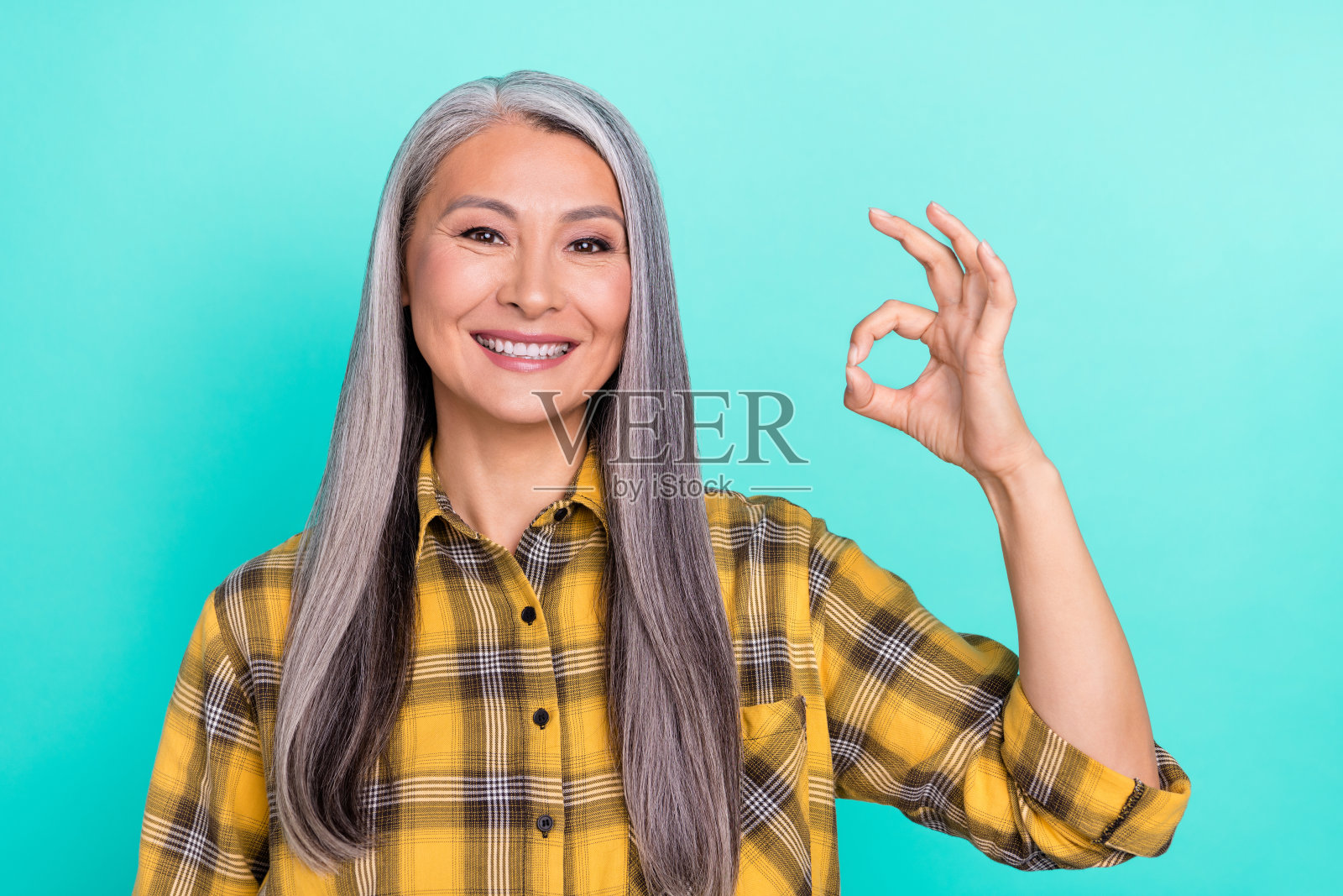 快乐的老年女士在青色背景前做出“好”的手势，展示选择和决定。照片摄影图片
