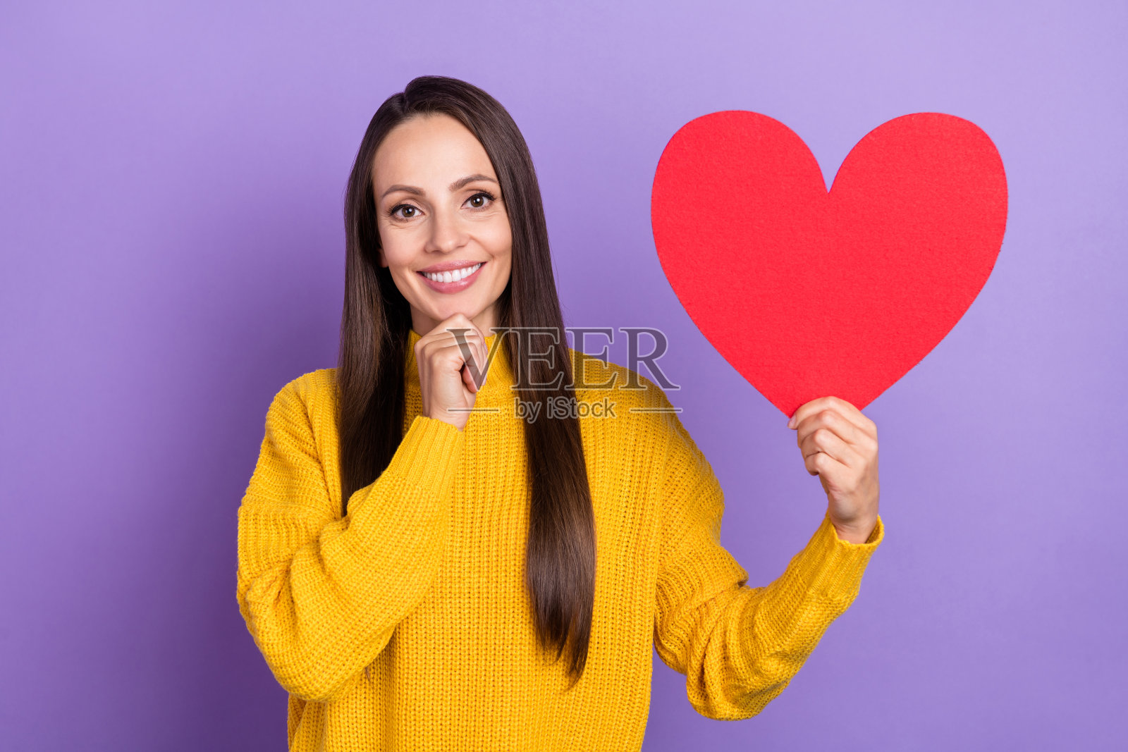 穿着黄色毛衣的美丽棕发成熟的女性在紫色背景前展示心形手势的照片照片摄影图片