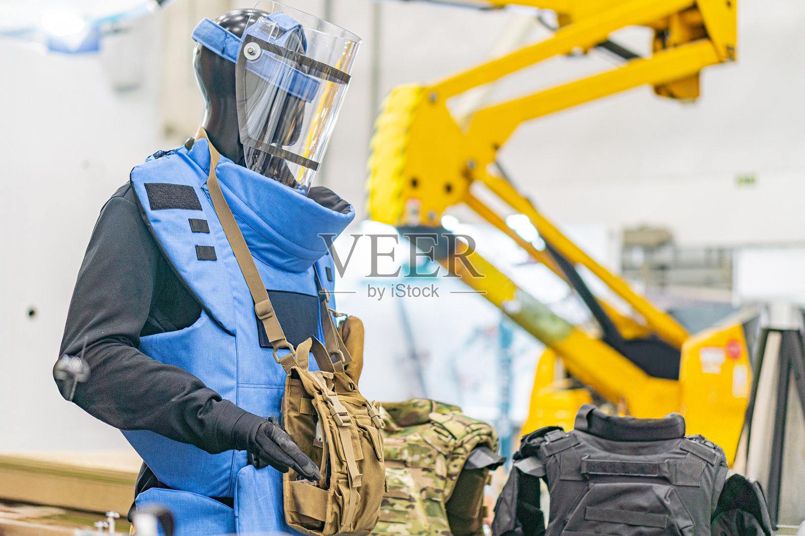 穿着蓝色防护服、戴着头盔和面罩的人，站在一个工业环境中，周围可见金属机械。由于面罩的遮挡，个人的面部被遮掩，暗示着佩戴了防护眼镜。照片摄影图片