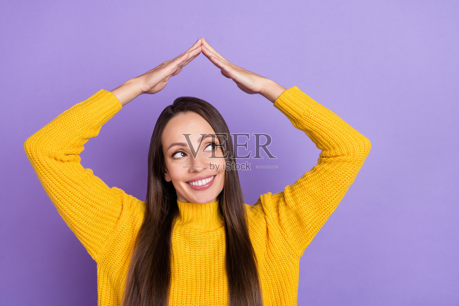 一位令人印象深刻的棕发年轻女士，双臂举起，穿着黄色毛衣，背景为紫色。照片摄影图片