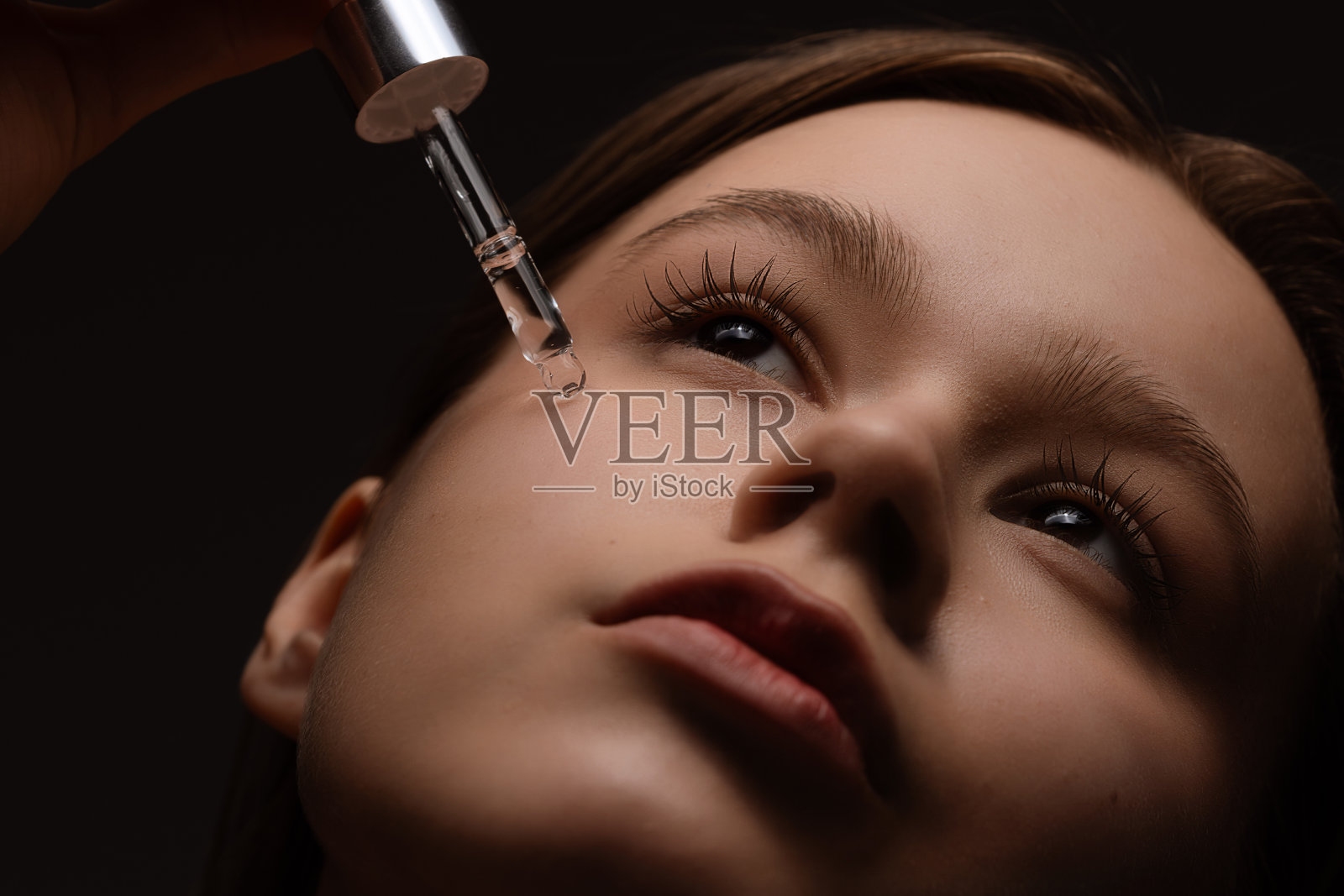 年轻女性使用滴管涂抹面部精华液进行护肤程序照片摄影图片