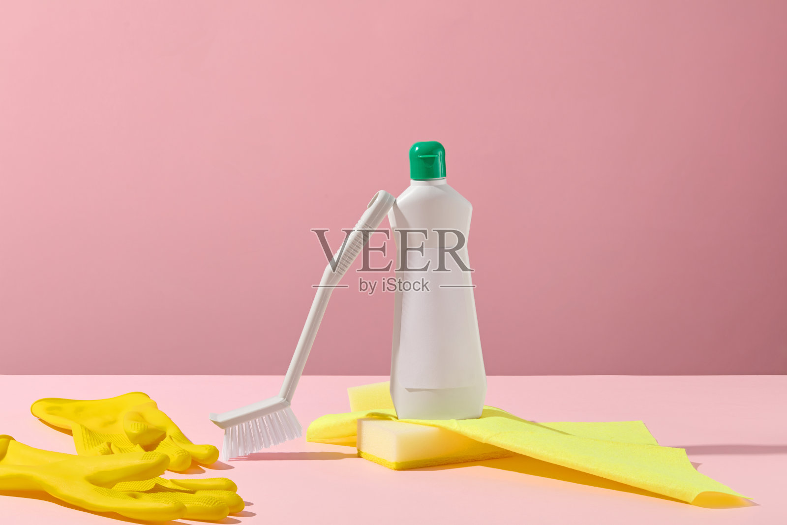 粉色桌子上的喷雾瓶和黄色手套，准备进行家庭清洁任务。柔和的粉彩色调，令人愉悦的布置。设计标签的模拟瓶。照片摄影图片
