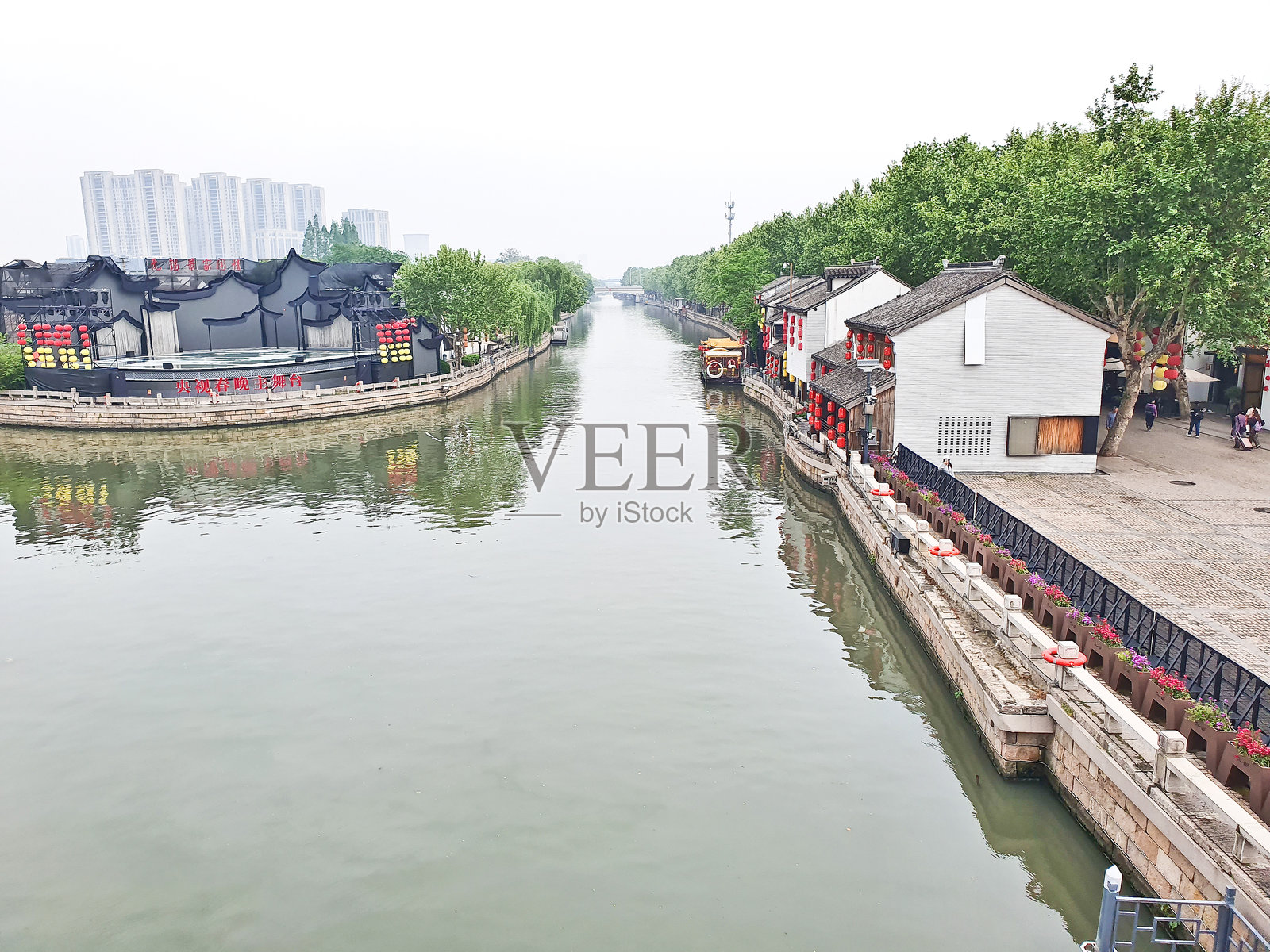 一个传统的运河小镇，红色灯笼、白色建筑，和一只在雾霭天空下宁静滑行的风景船照片摄影图片