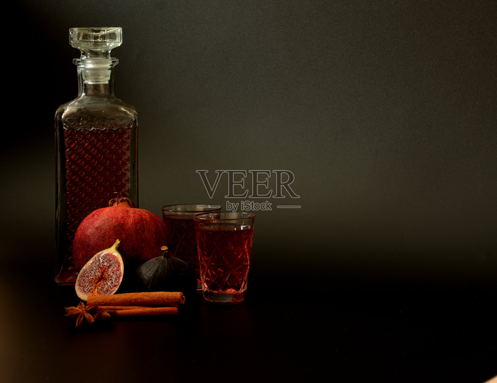 无花果石榴利口酒，搭配肉桂和八角，背景为黑色，强烈的自制酒在水晶酒具中，旁边是调料和成熟的水果。照片摄影图片