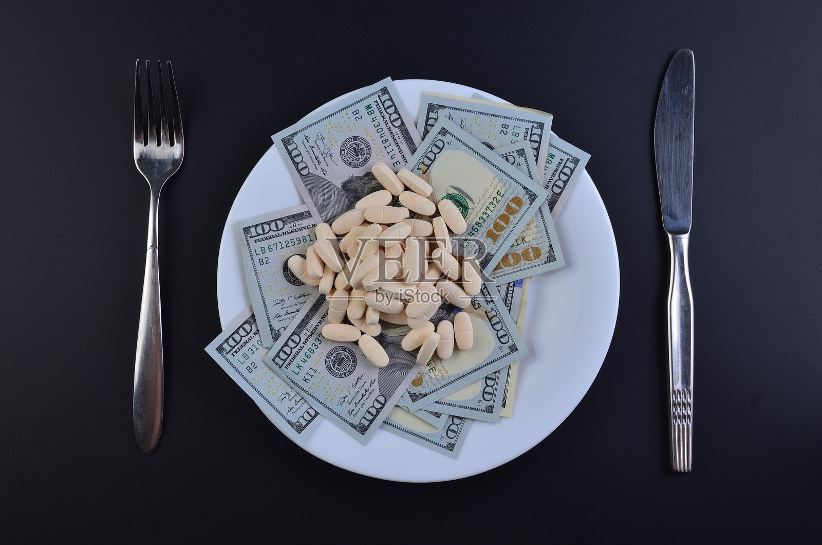 黑色背景上，盘子里放着美元钞票、药丸和餐具。照片摄影图片