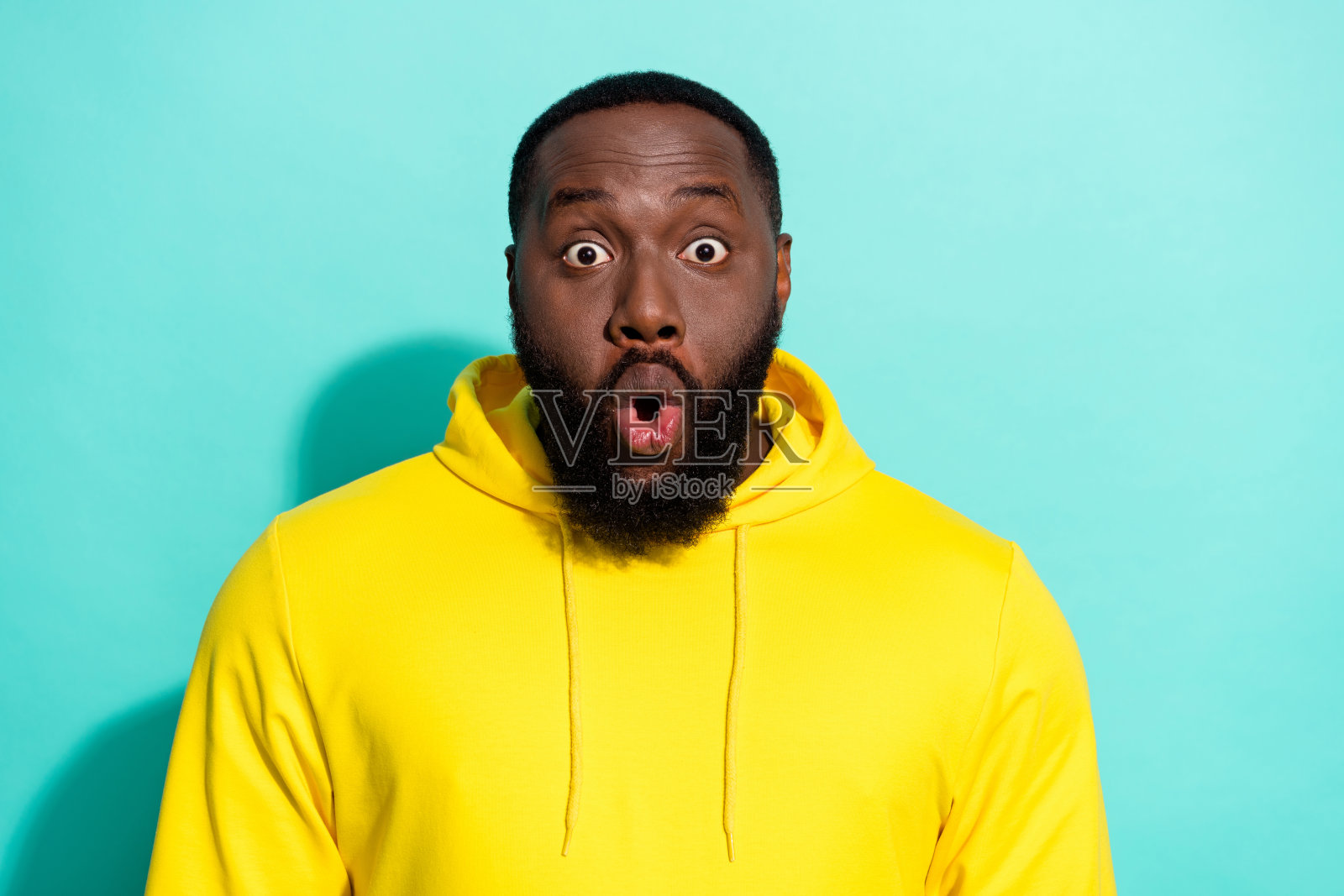 穿着黄色连帽衫的棕发时尚年轻男子，张嘴，背景为青色。照片摄影图片