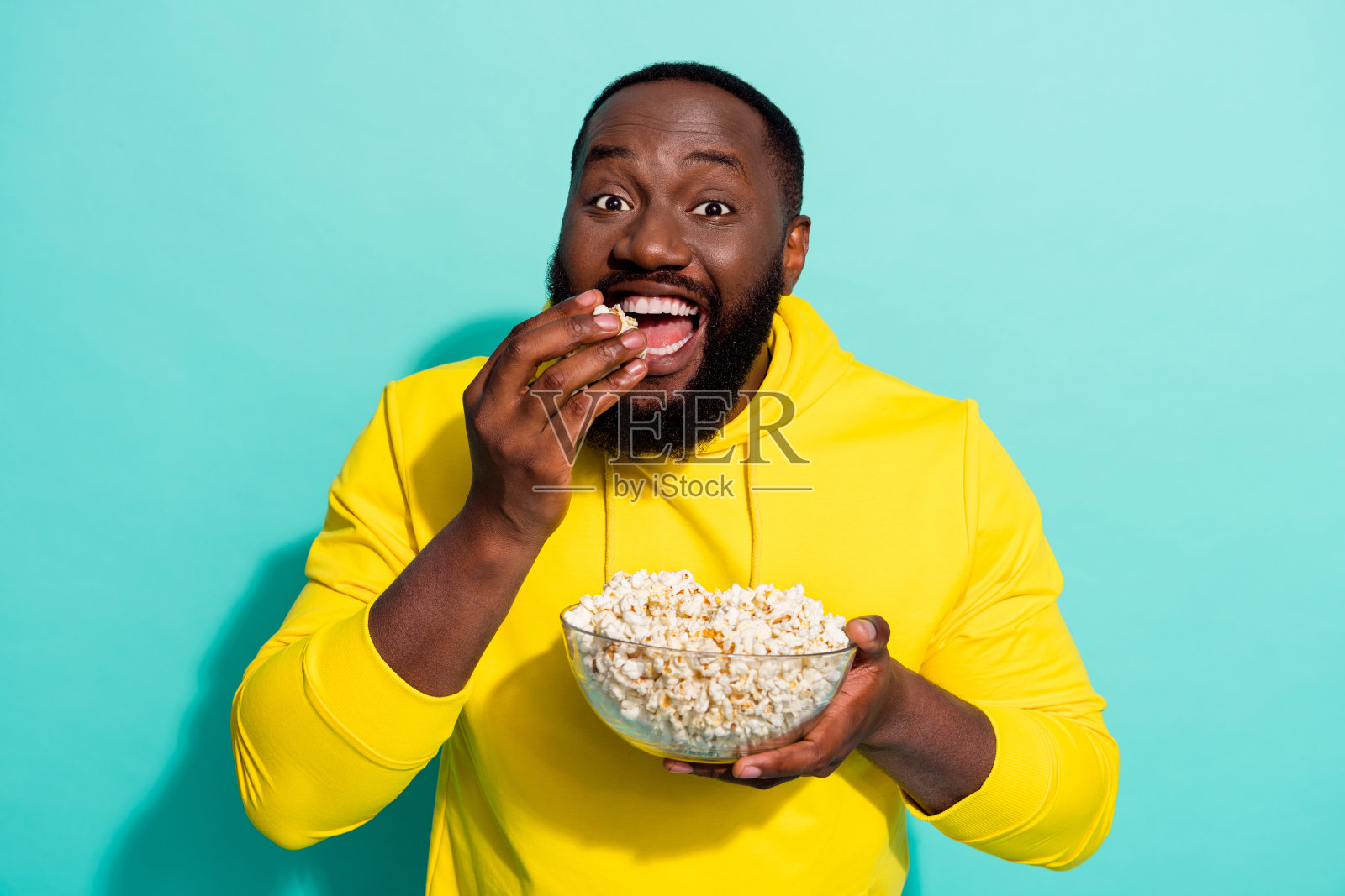 兴奋的积极男孩，沉迷于电影，吃着爆米花，穿着毛衣，背景为青色。照片摄影图片