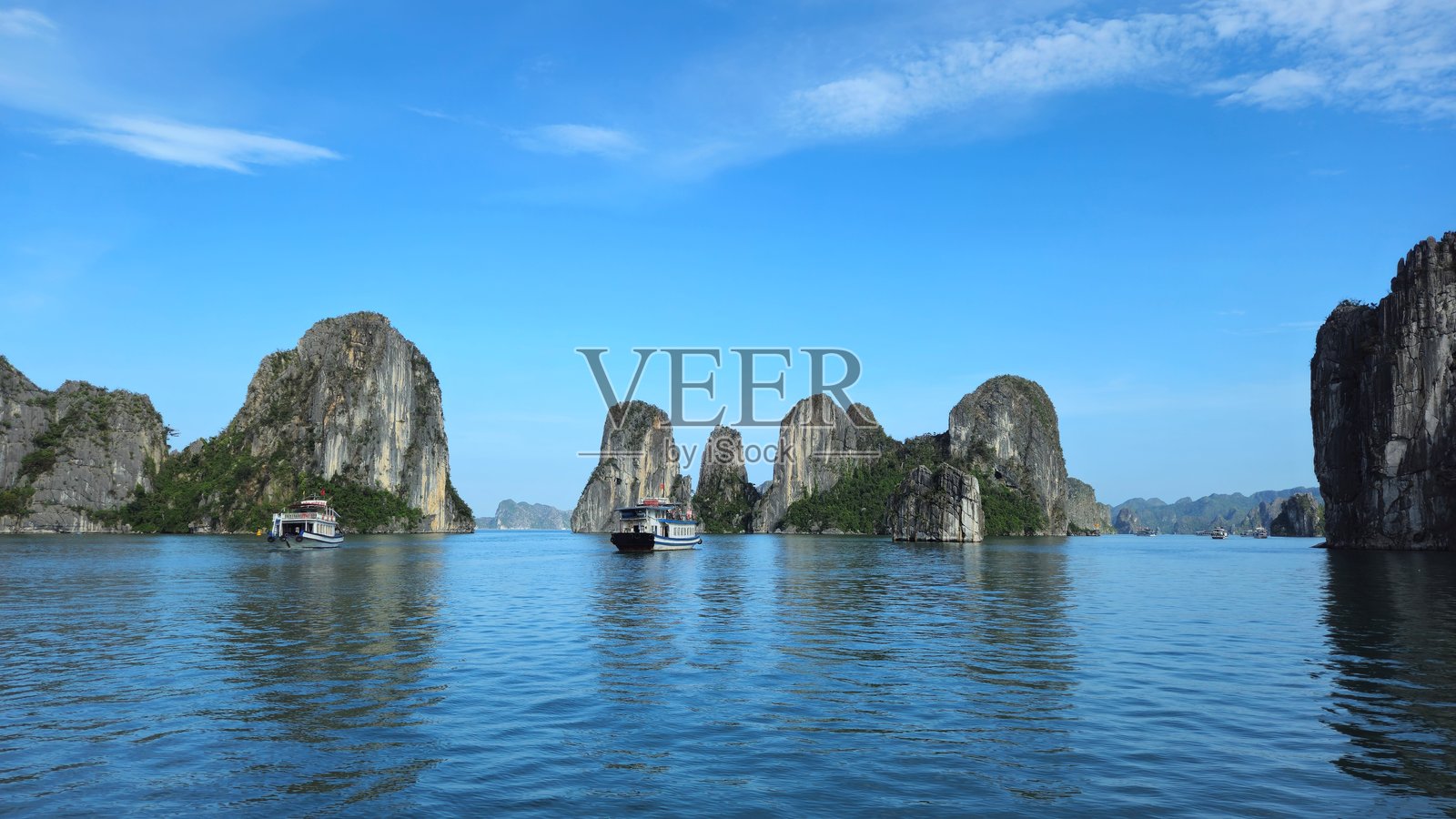 雄伟的石灰岩地貌在越南下龙湾宁静的水面上倒映，映衬着晴朗的阳光明媚的天空。照片摄影图片