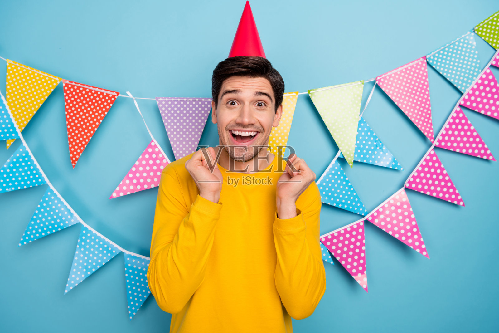 年轻男子在蓝色背景下庆祝狂欢派对，举起拳头欢呼，庆祝中奖。照片摄影图片