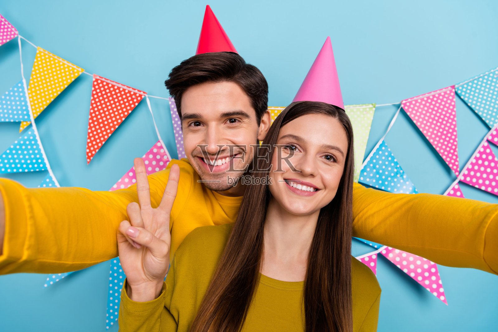 可爱的夫妻在节日场合自拍，做出V字手势，背景为蓝色。照片摄影图片