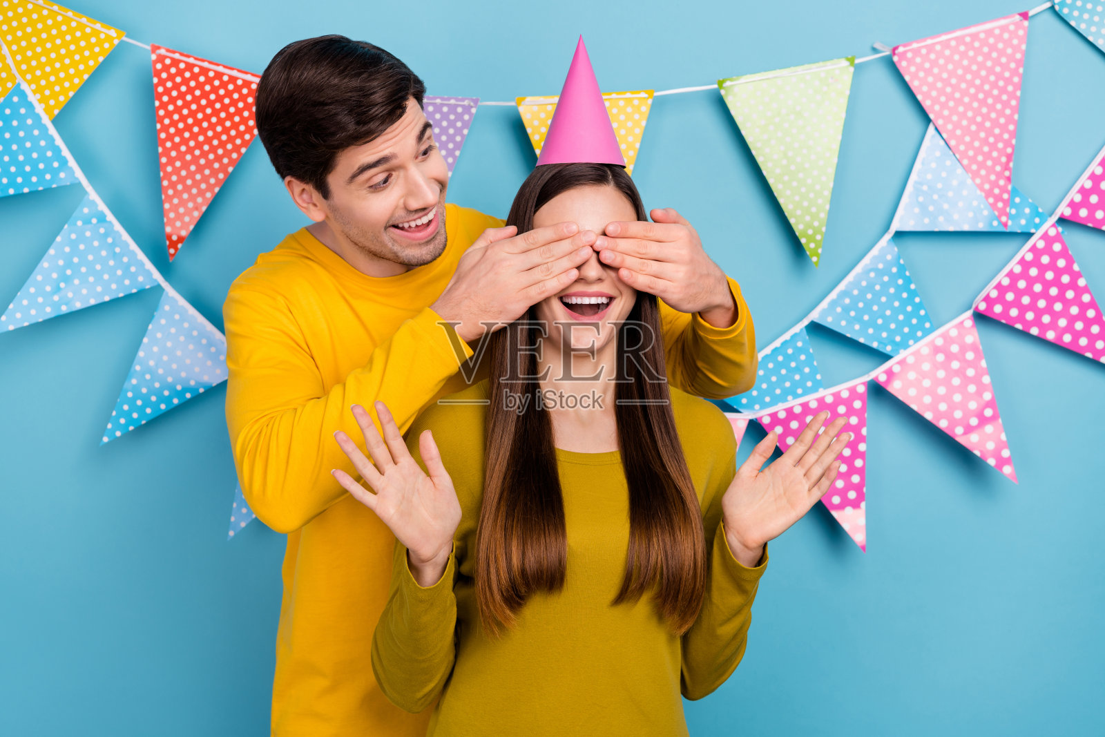 惊讶的女士，她的配偶遮住眼睛，准备许愿梦幻包裹，狂欢节庆祝活动，背景为蓝色。照片摄影图片