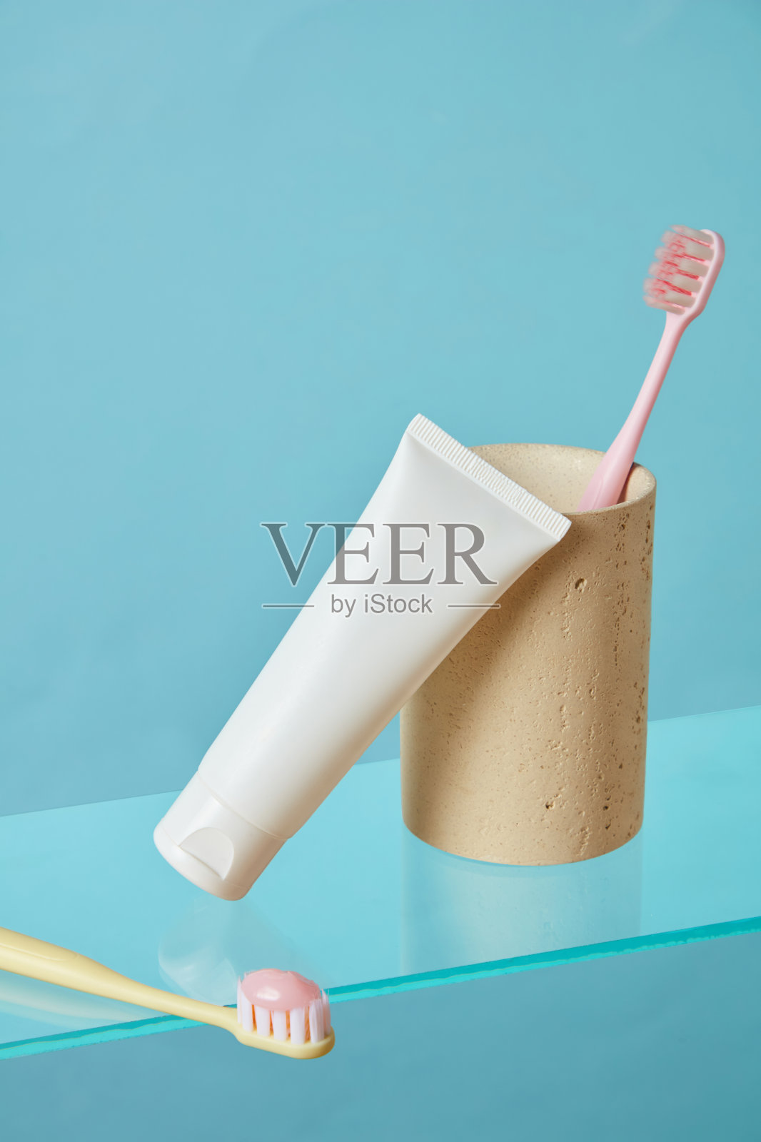 牙刷和牙膏管垂直排列在绿色地板上，背景为黄色。现代简约布局，明亮的柔和色调用于产品展示。照片摄影图片