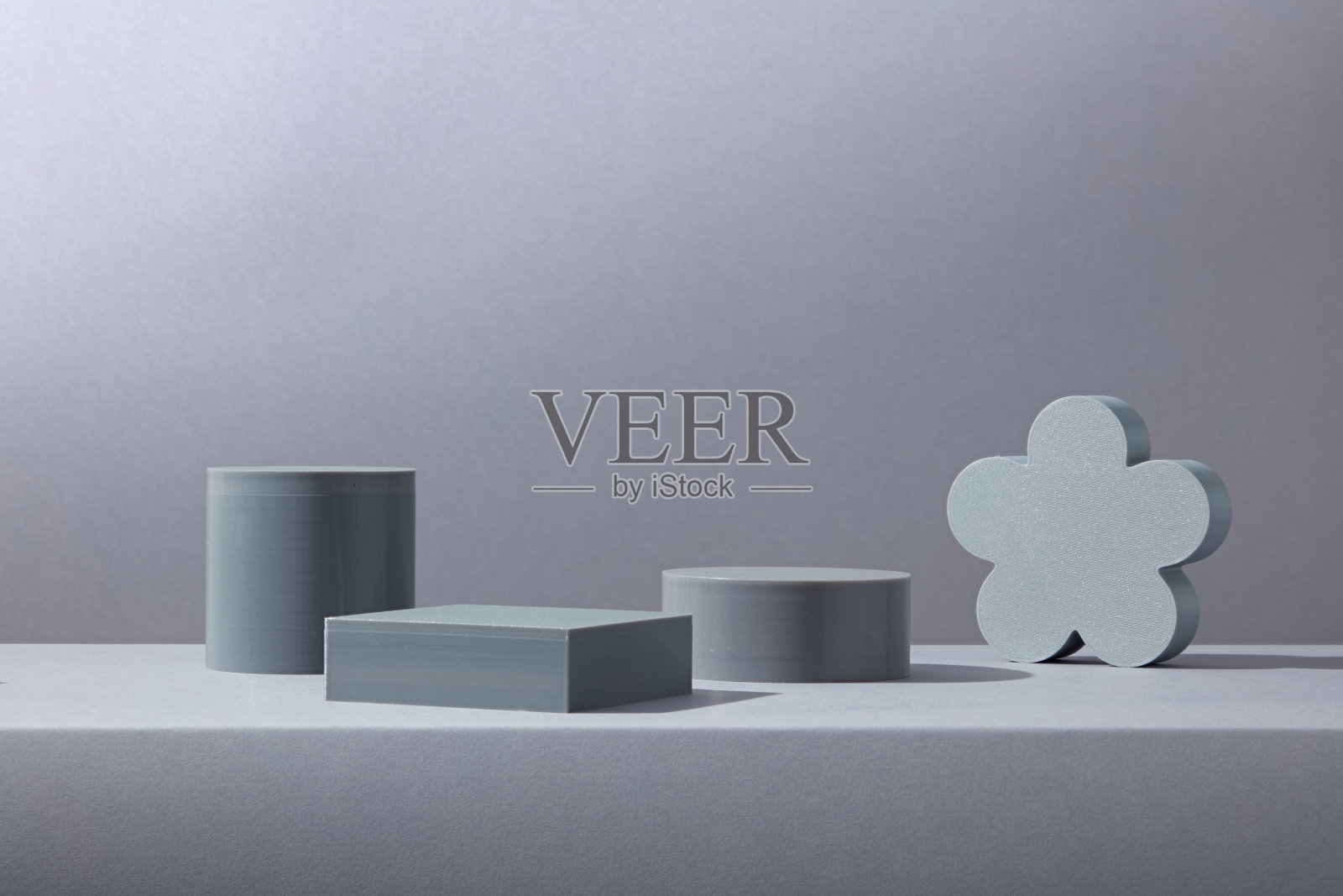 各种灰色讲台，包括圆柱体和花卉剪影形状，置于中性色灰色底座上。适合化妆品或编辑产品的创意展示。照片摄影图片
