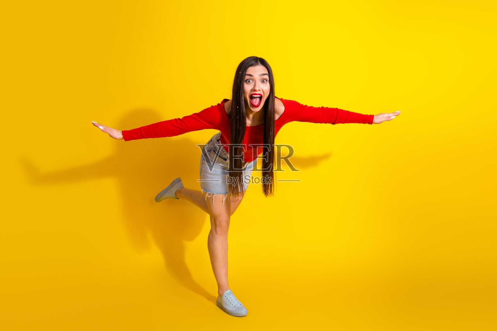 年轻女性穿着休闲服装，在黄色背景前俏皮地摆姿势，展现出活力与时尚感。照片摄影图片