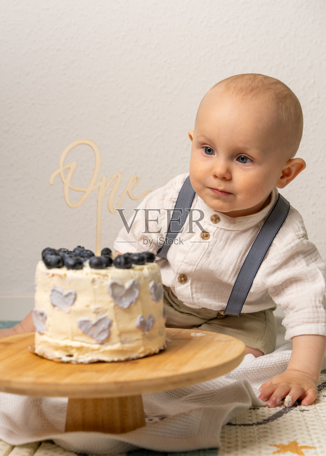 可爱的一岁男婴坐在小生日蛋糕旁。微笑的孩子庆祝他的第一个生日。甜美而喜庆的时刻，完美适合家庭、童年和庆祝主题。照片摄影图片