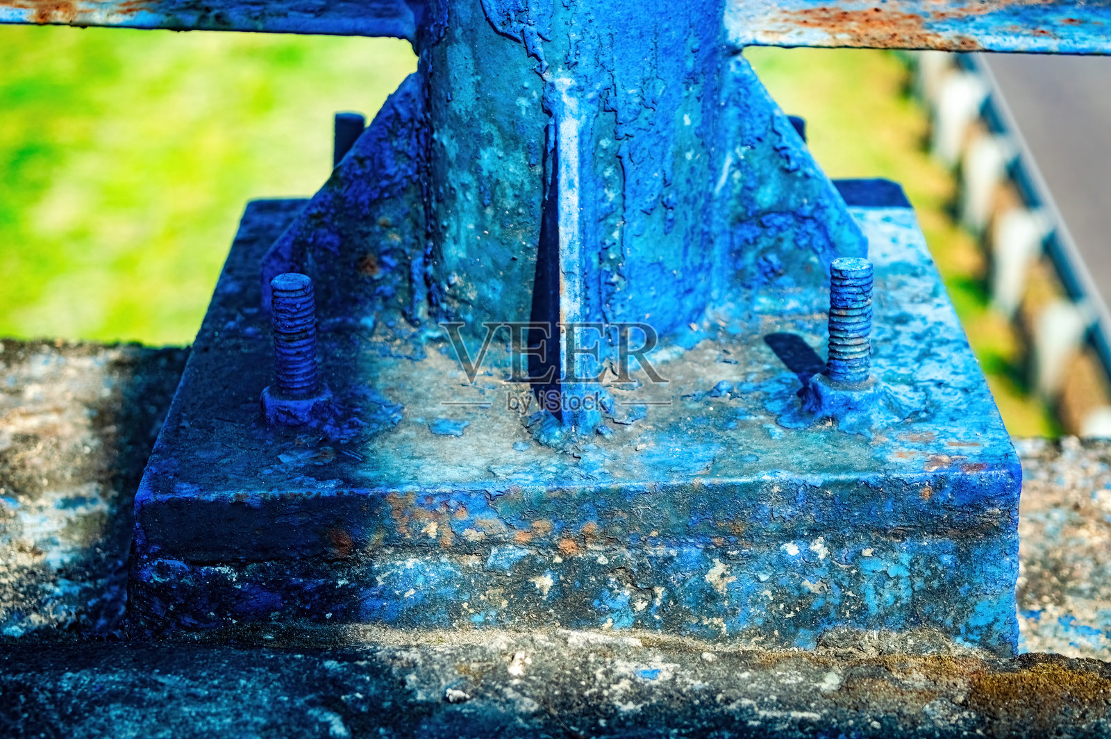 一块严重风化的蓝色金属底座，用生锈的螺栓固定在混凝土块上，表面有剥落的油漆和老化的迹象。展现了工业衰退、韧性以及受损纹理的美感。照片摄影图片