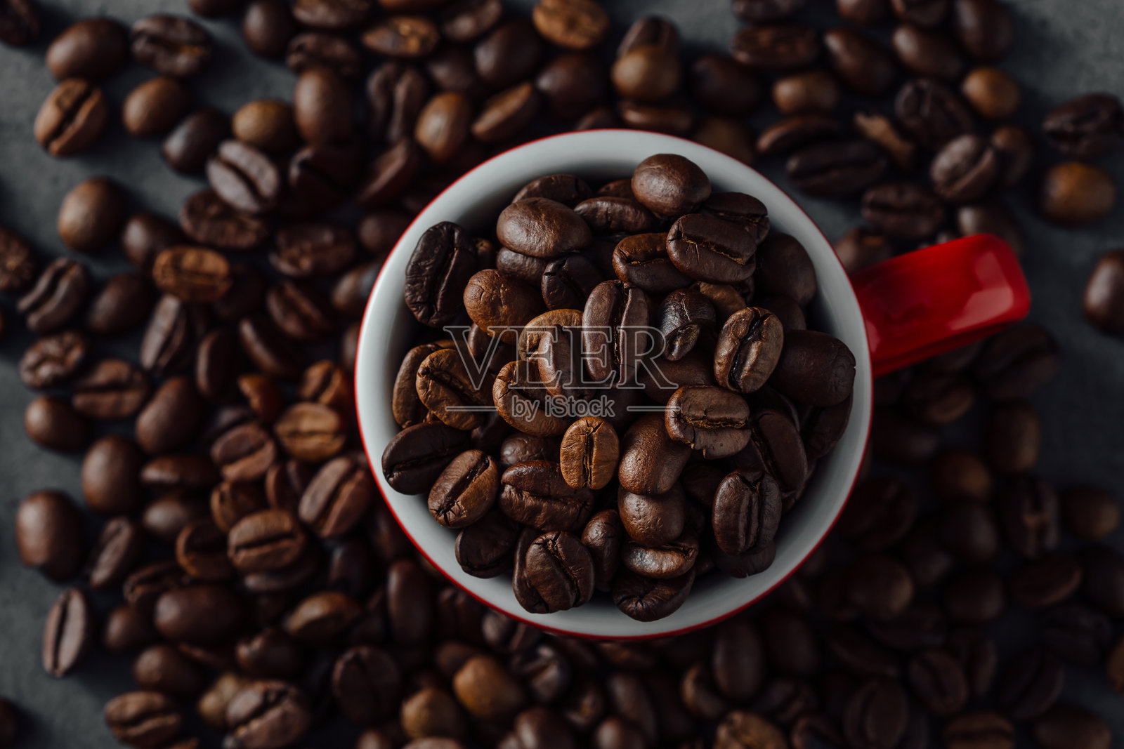 新鲜烘焙的咖啡豆在红色杯子里，周围是咖啡渣照片摄影图片