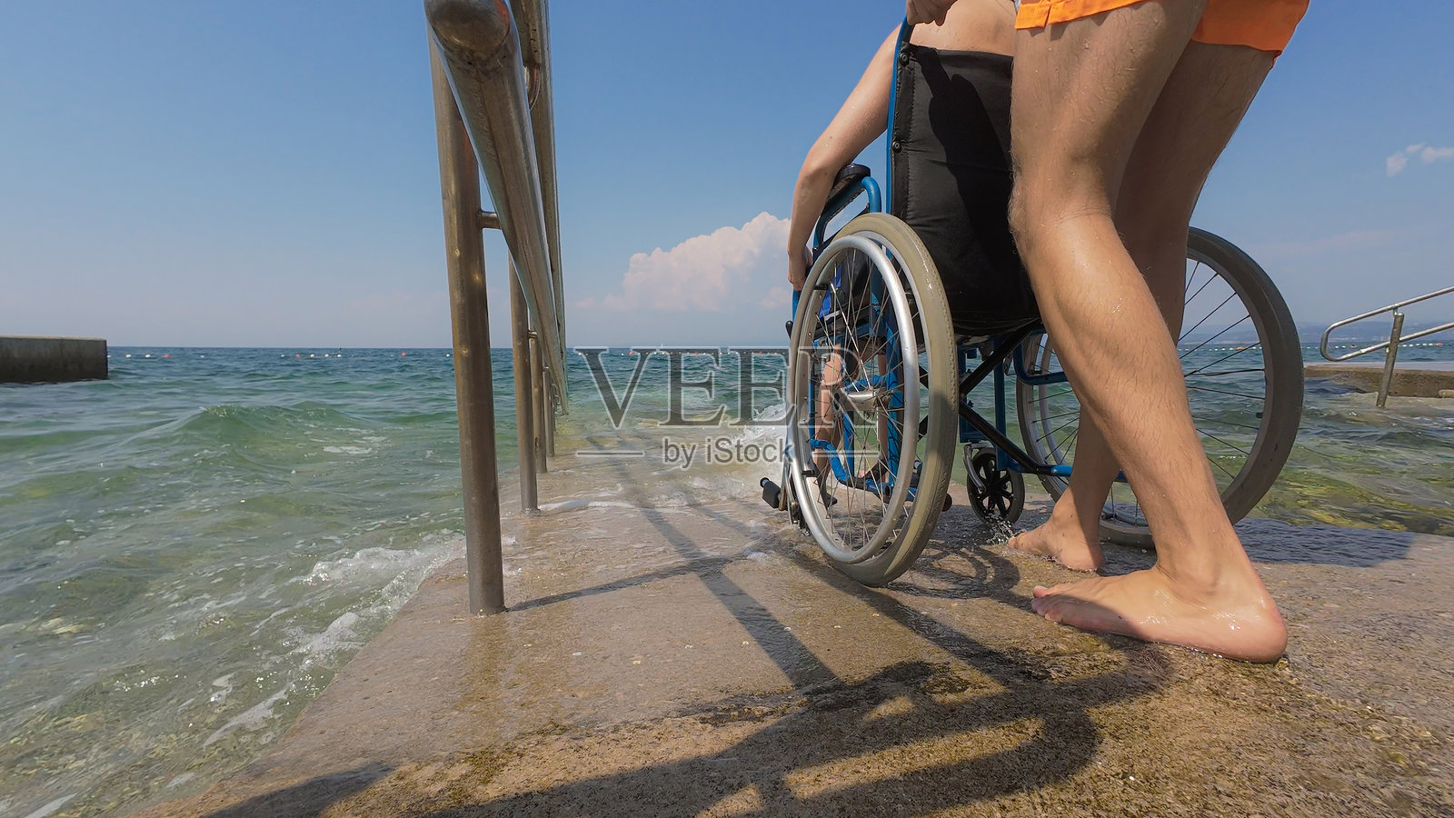 救生员帮助一位残疾女性通过轮椅坡道进入水中照片摄影图片