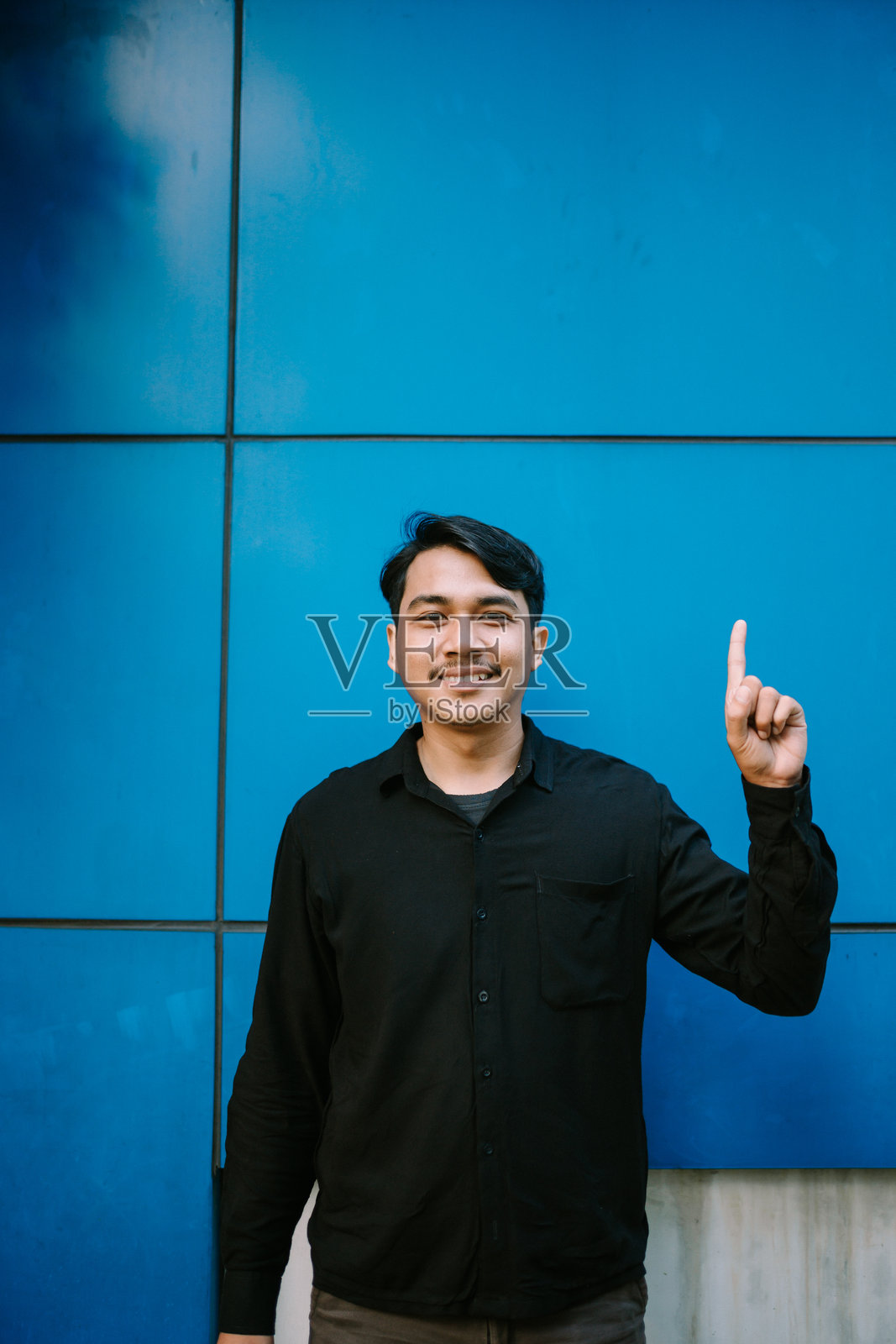 热情的男子在明亮的蓝色瓷砖背景前指向上方照片摄影图片